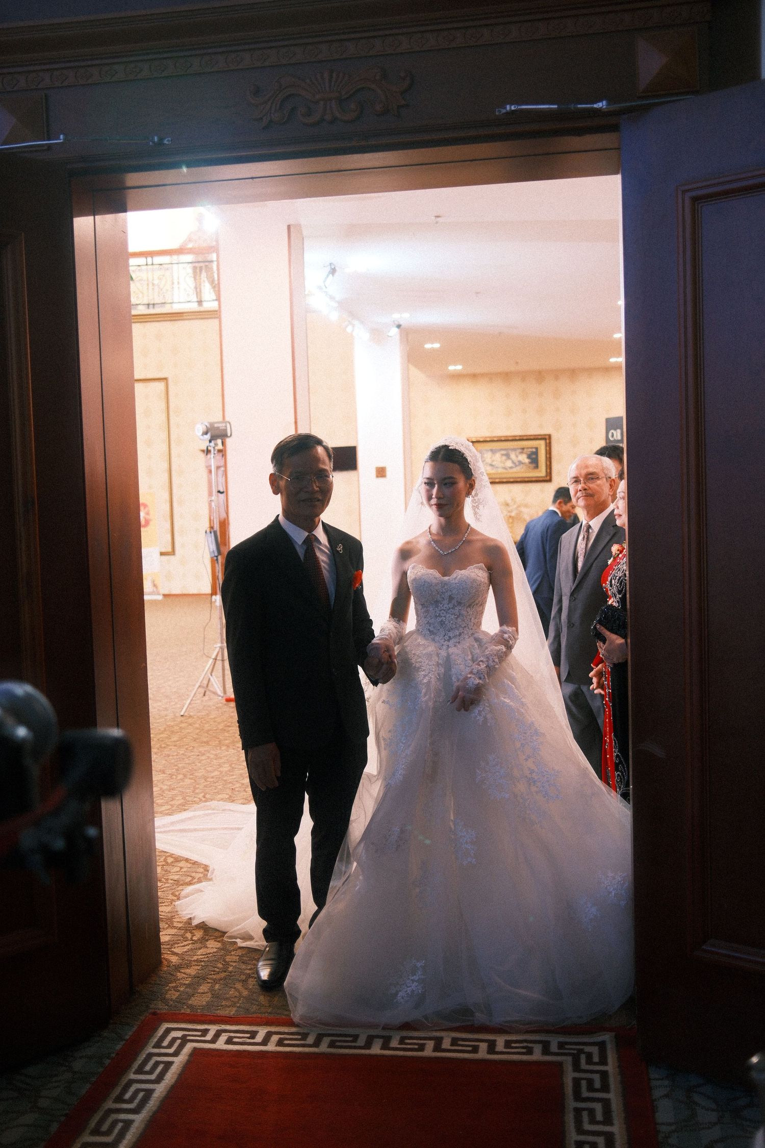 Bride in white ball gown wedding dress walks through doorway with escort during elegant wedding ceremony.