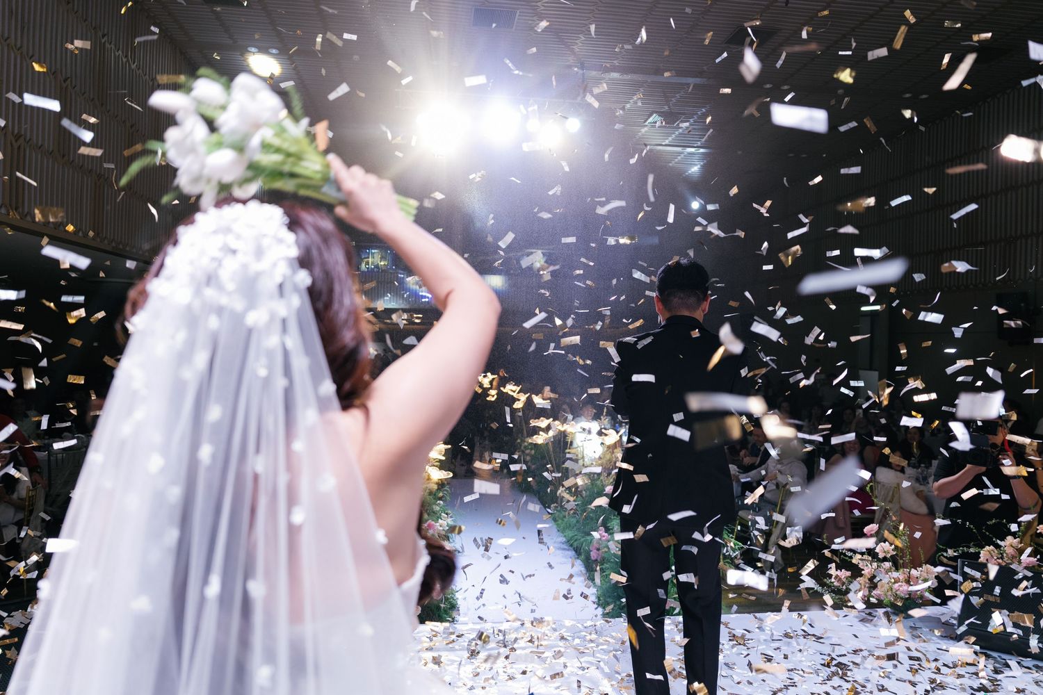 Bride and groom celebrate with confetti at elegant wedding reception, bride holding bouquet in white veil.