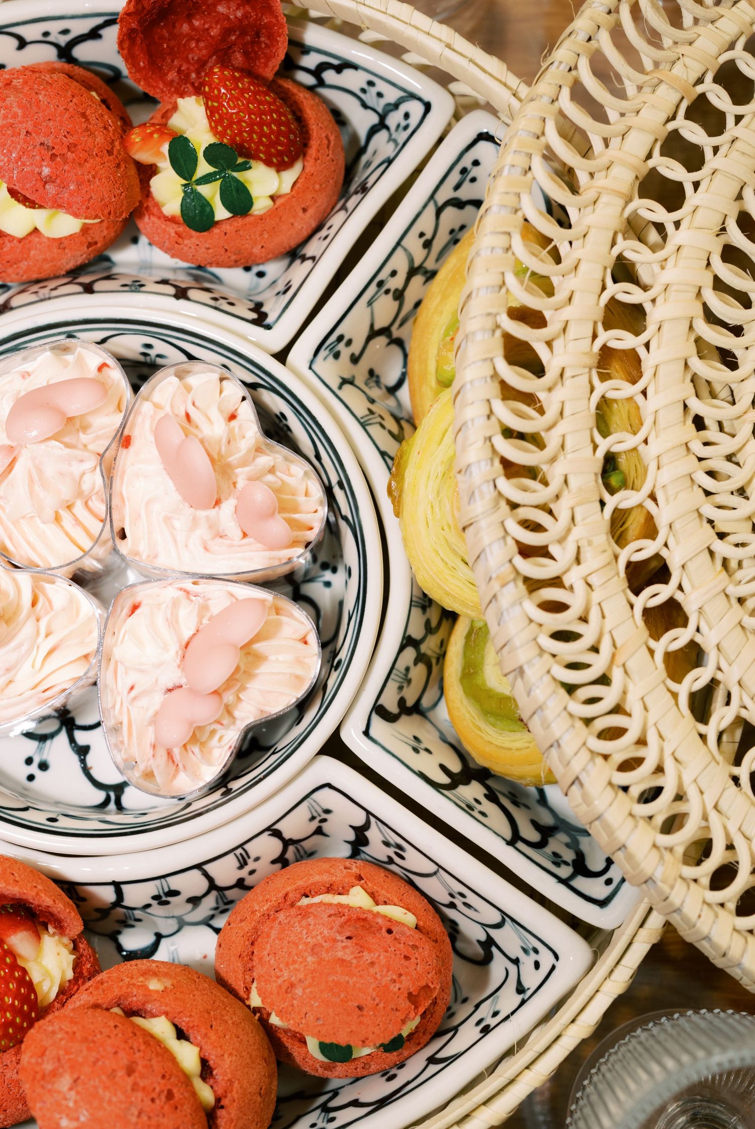 Elegant dessert platter with red macarons, strawberry tarts, and pink cream pastries on decorative blue and white ceramic.