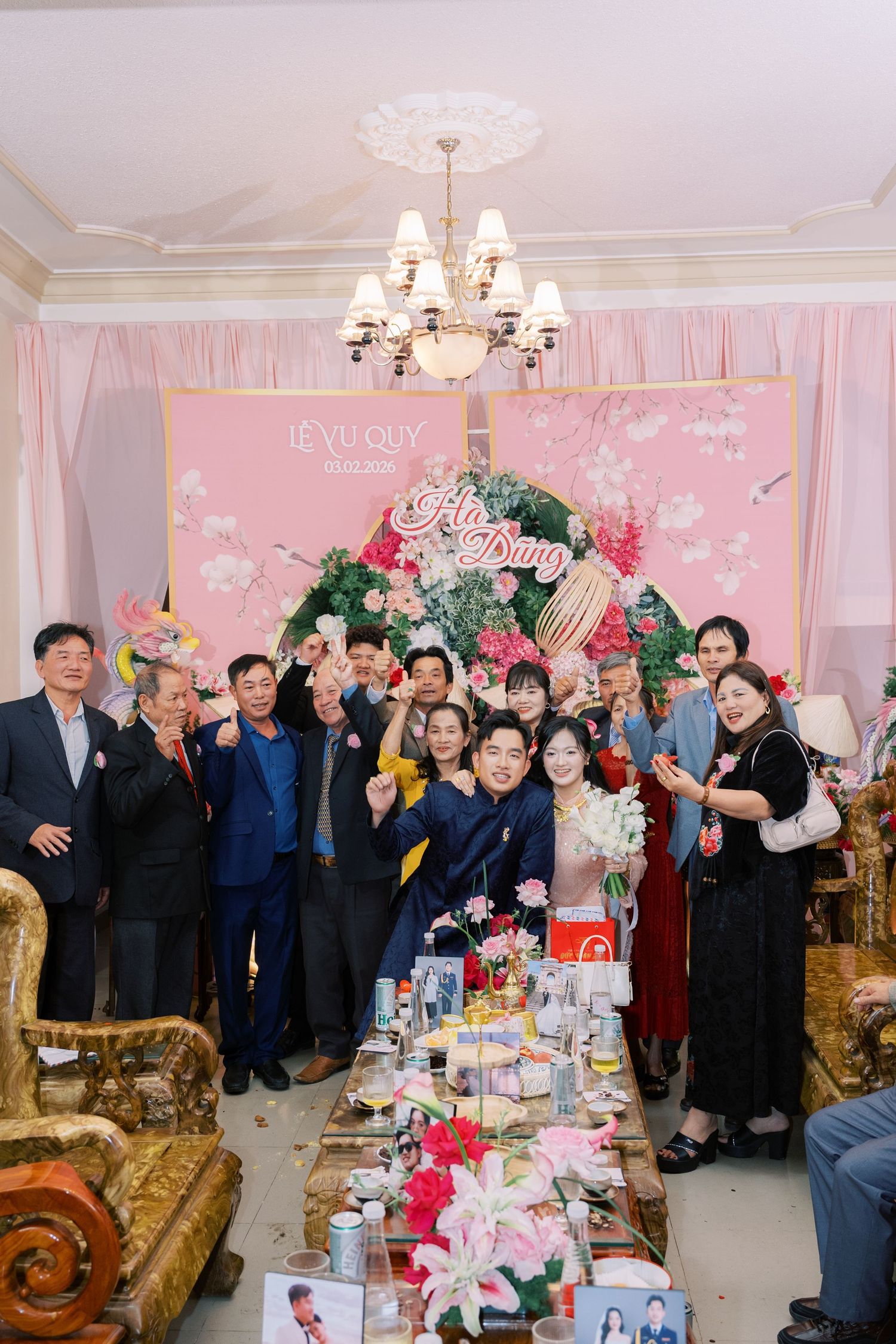 Guests pose together at a Vietnamese Le Vu Quy wedding ceremony in front of a pink floral backdrop.