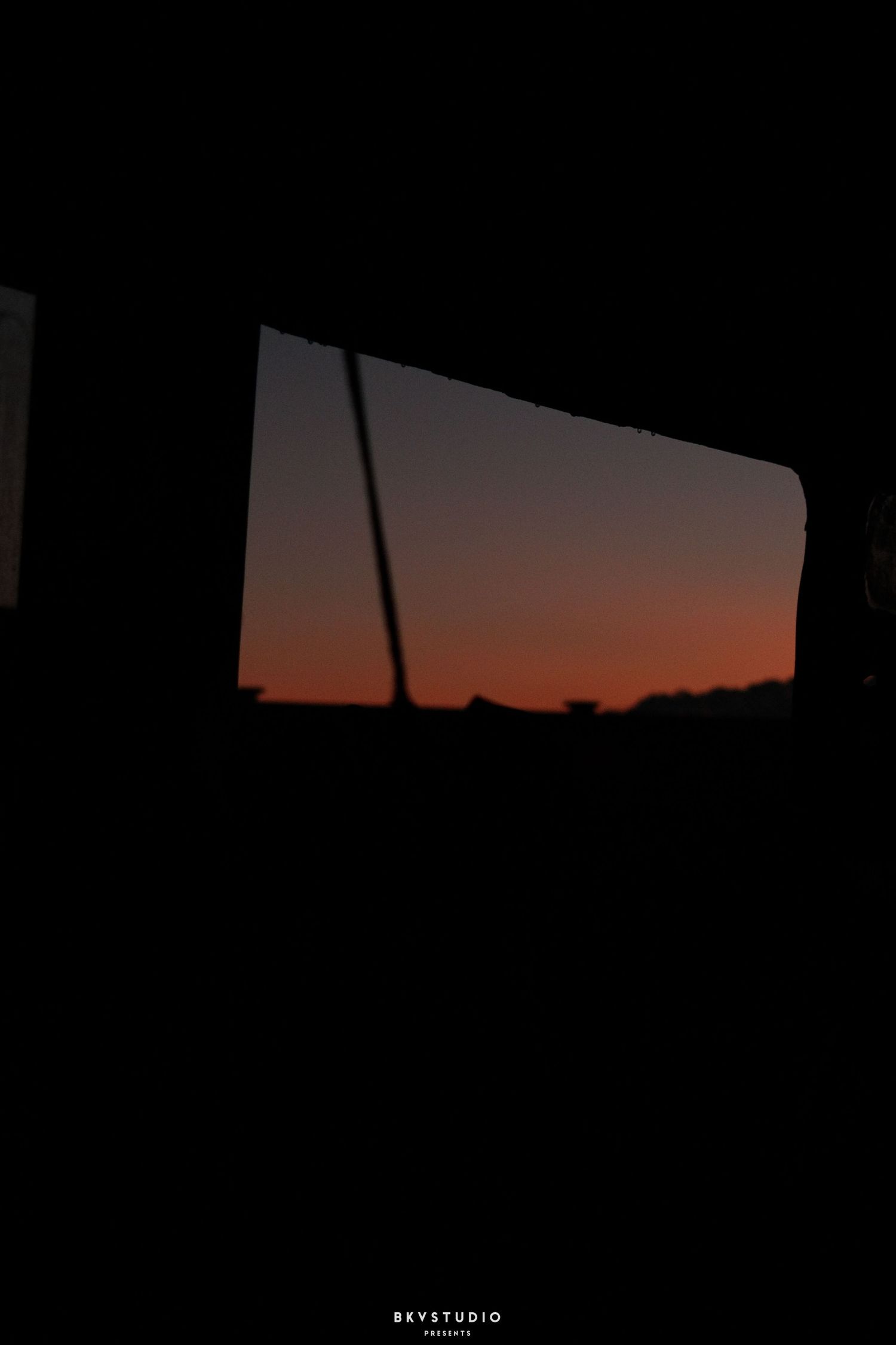 Silhouette view through a car window revealing a stunning orange and red sunset sky at dusk.