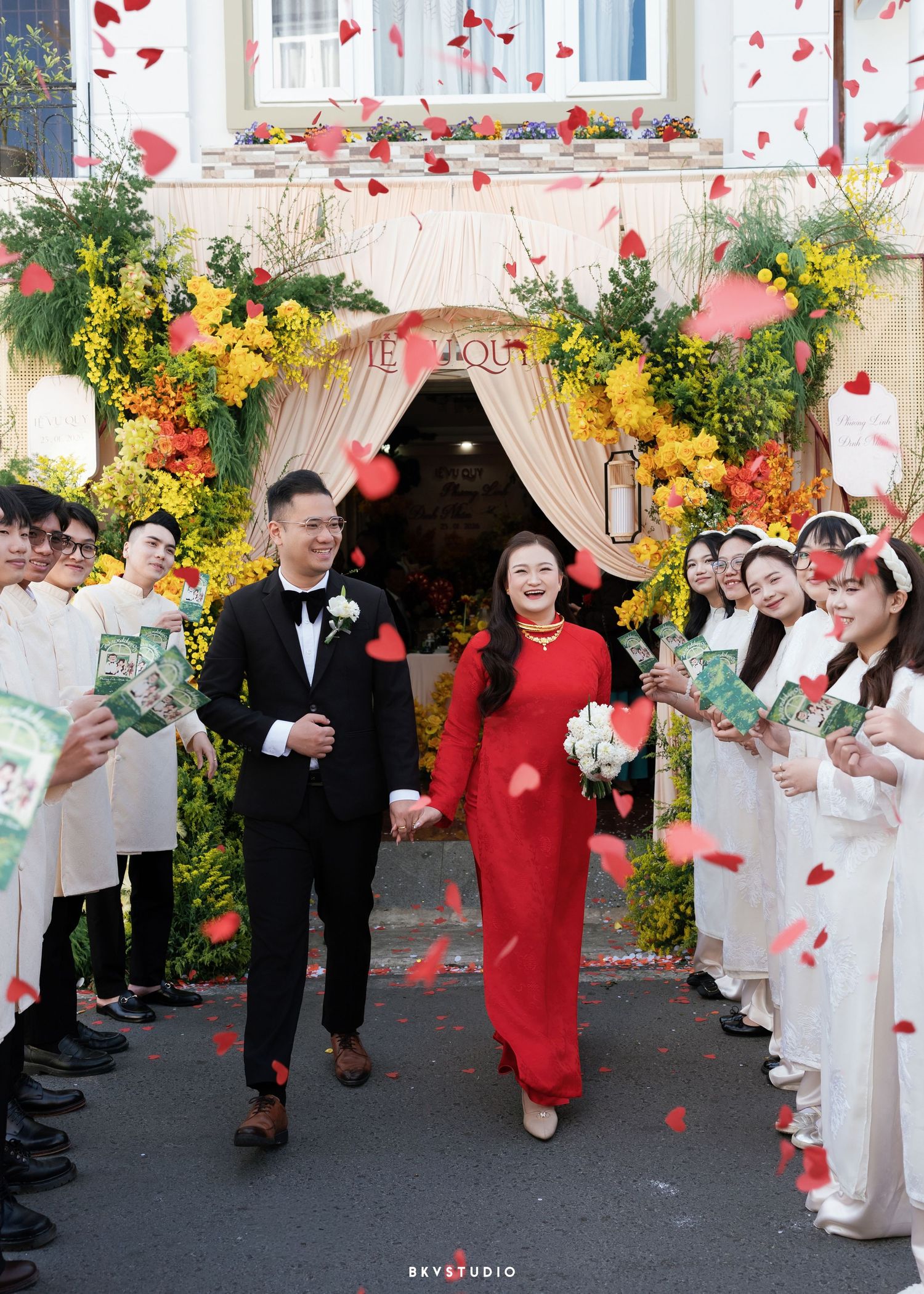 Vietnamese couple in traditional ao dai attire walks through flower petal shower at elegant wedding ceremony.