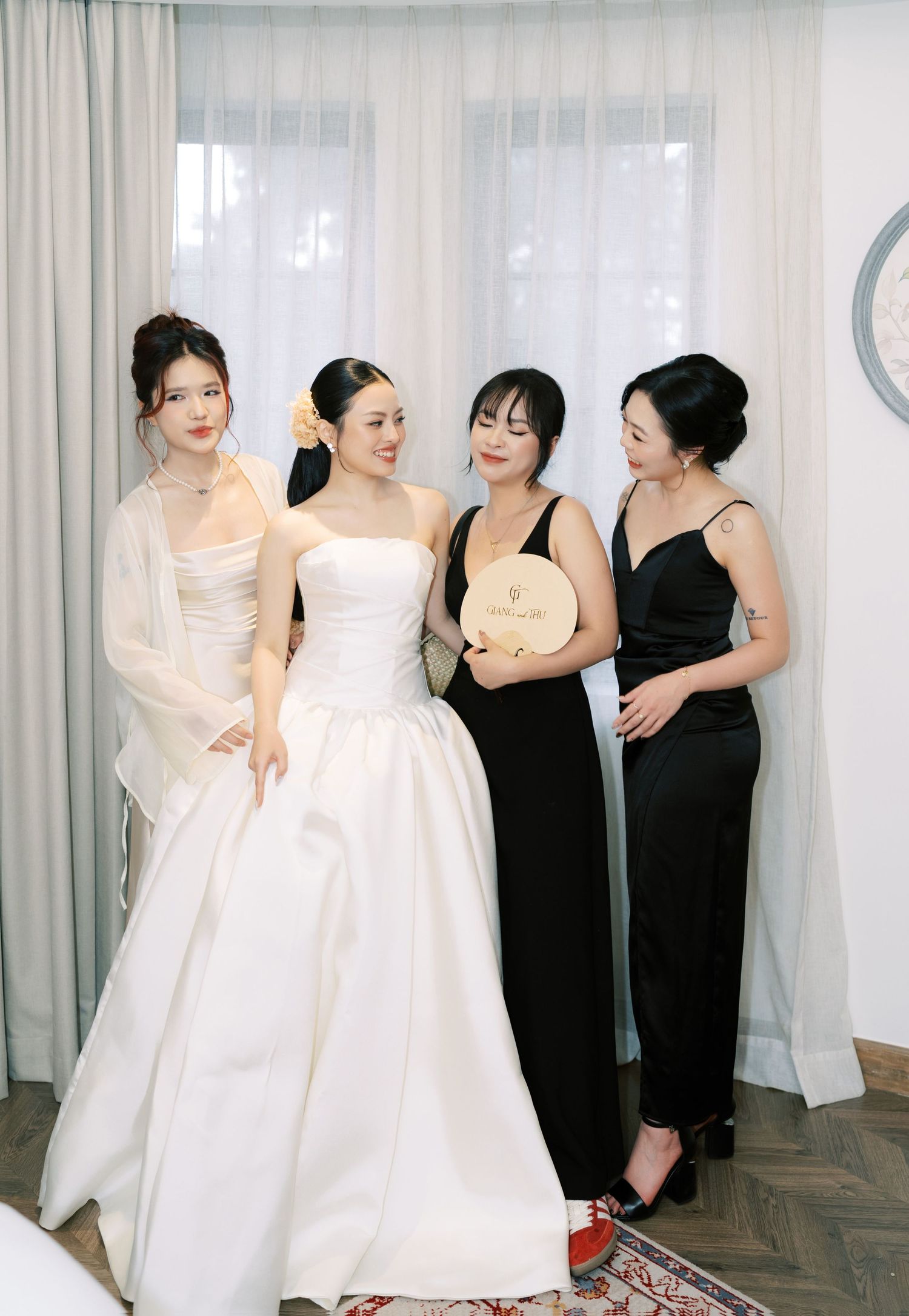Bride in elegant white strapless ball gown posing with three bridesmaids in black dresses indoors.