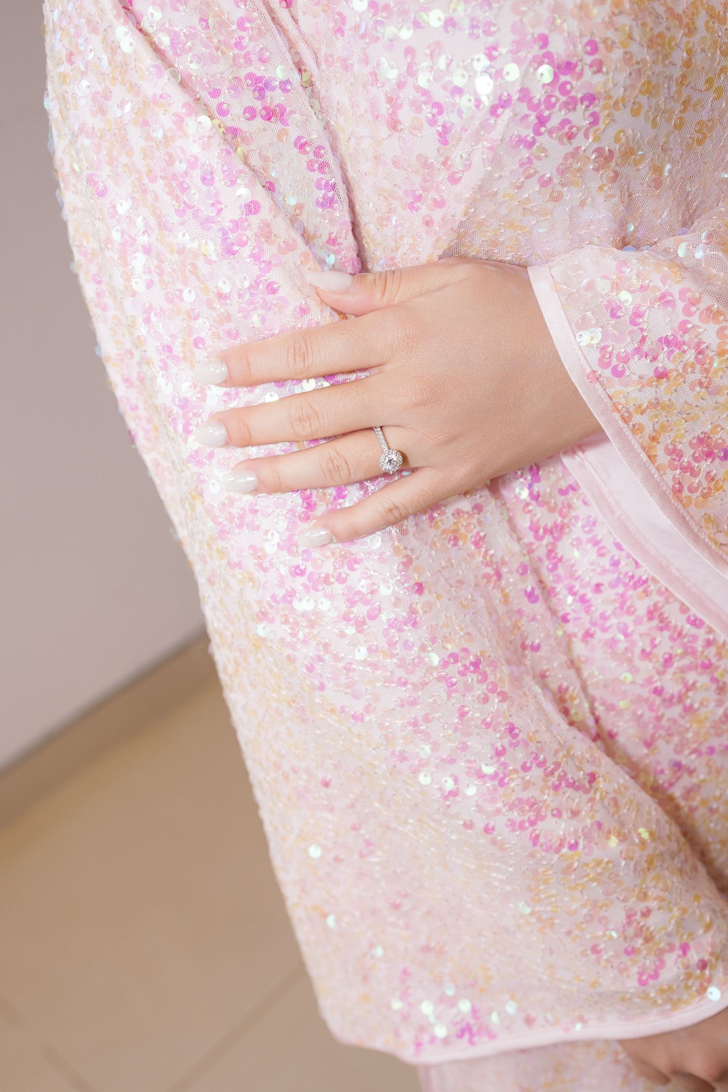 Close-up of a diamond engagement ring on a hand against a pink sequined dress.