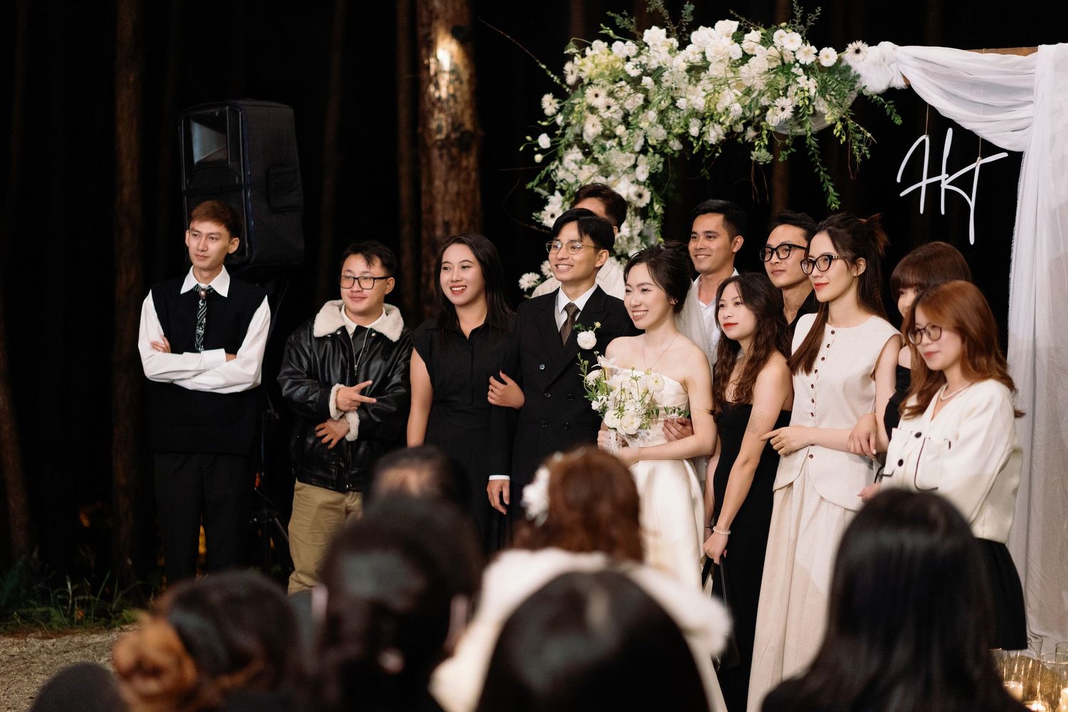 Wedding party poses under floral arch with white blooms at elegant indoor ceremony.