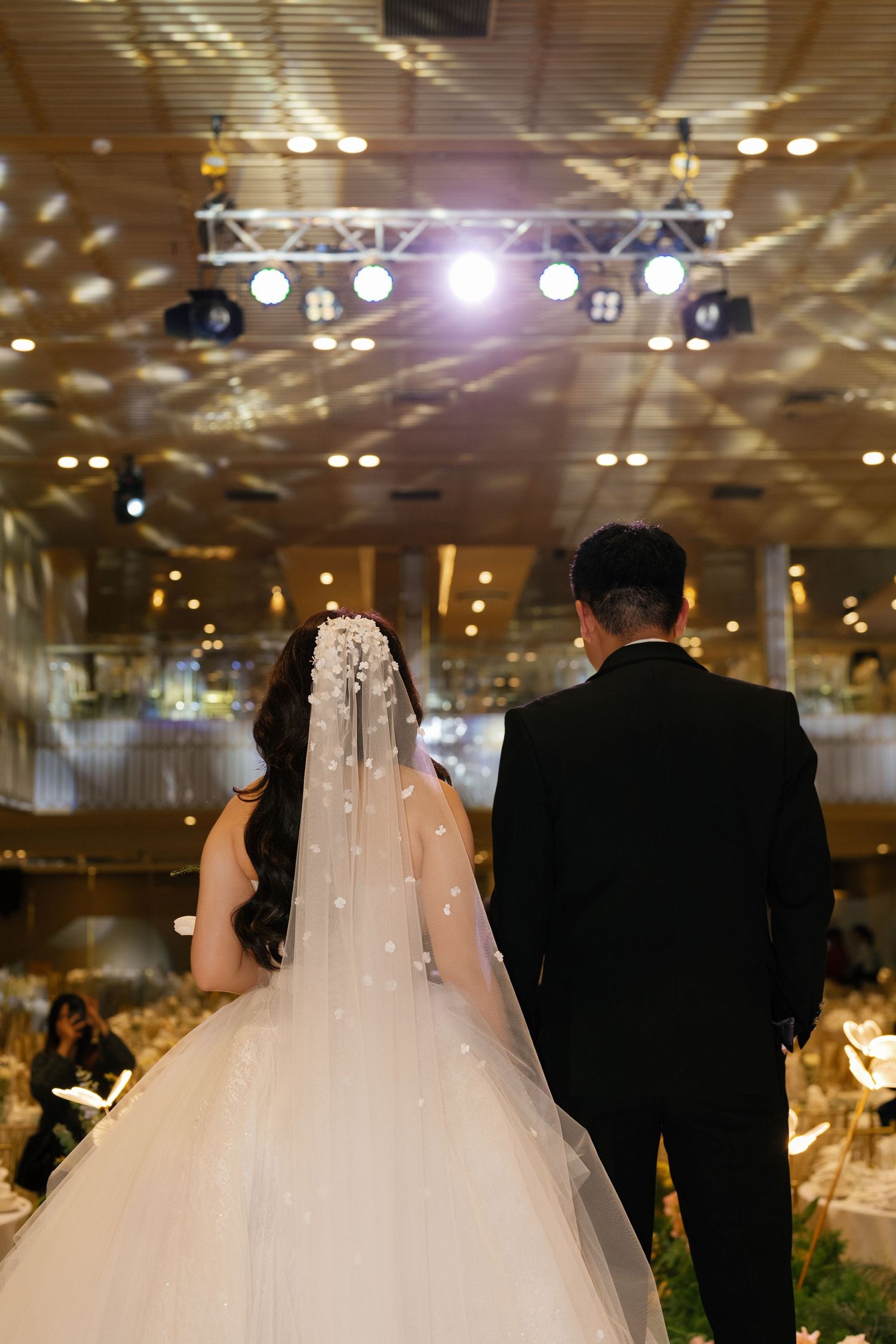 Bride and groom seen from behind entering a grand wedding reception hall with sparkling lights and elegant decor.