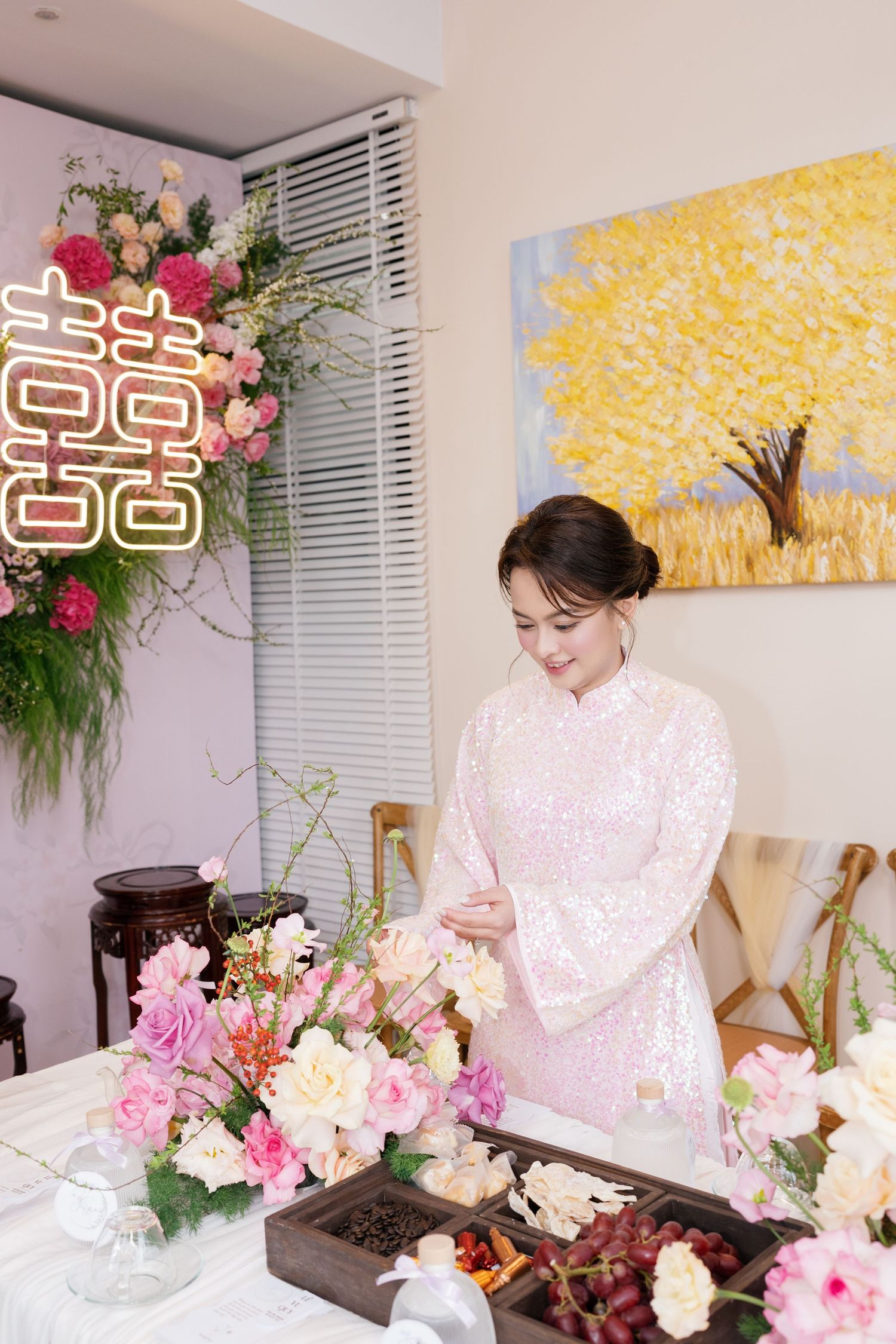 Vietnamese bride in pink ao dai arranges flowers at traditional wedding ceremony with double happiness symbol.