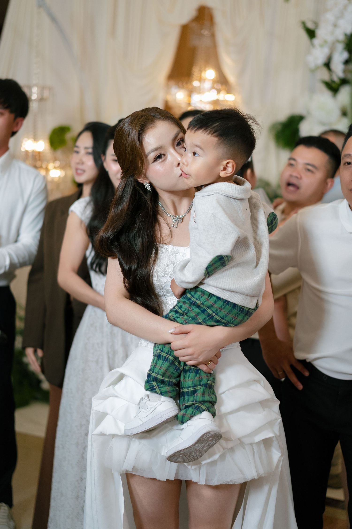Woman in white dress kissing a young boy at an elegant wedding reception event.