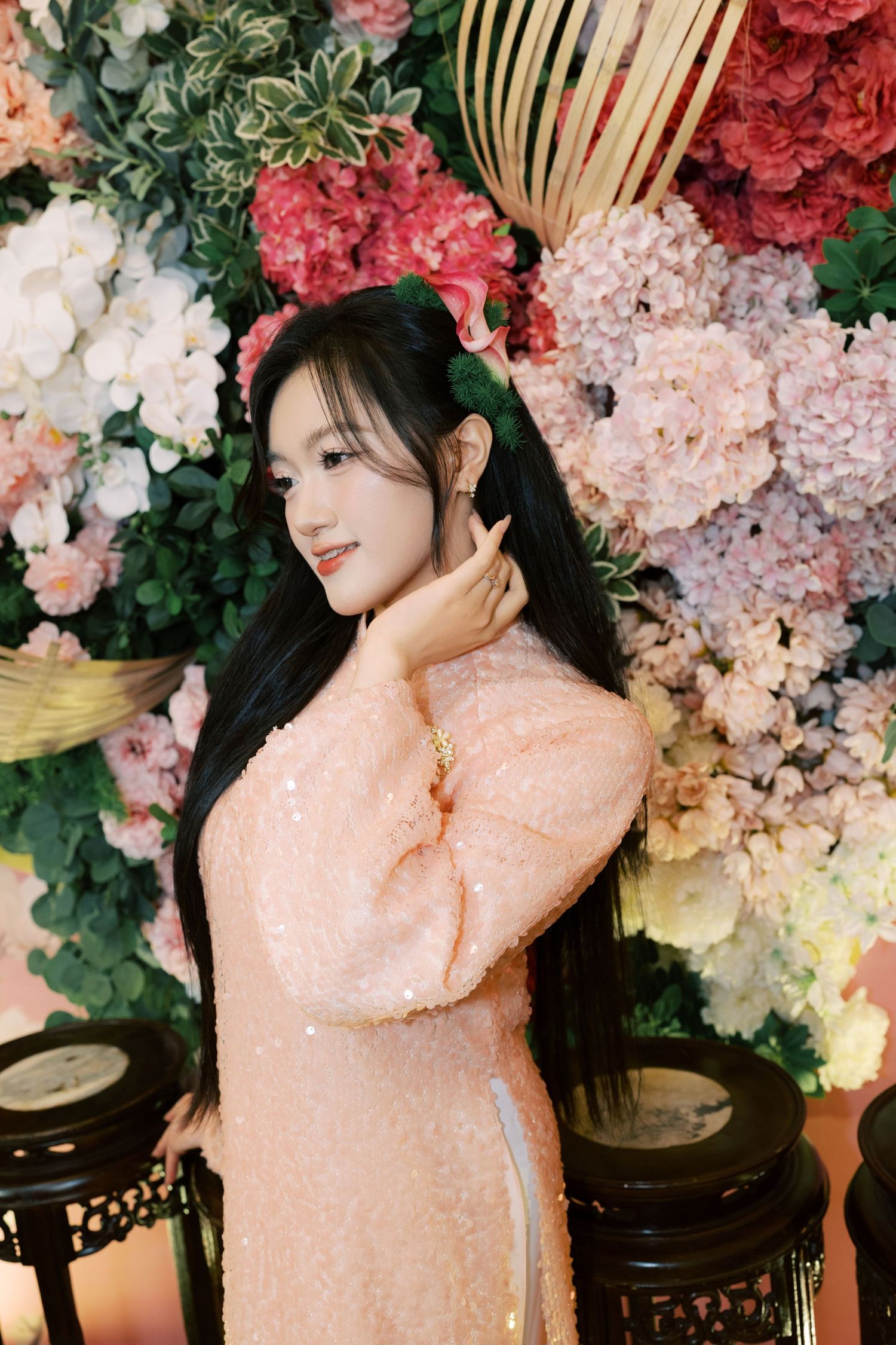 Young woman in pink sequin dress posing gracefully before colorful floral backdrop with hydrangeas.