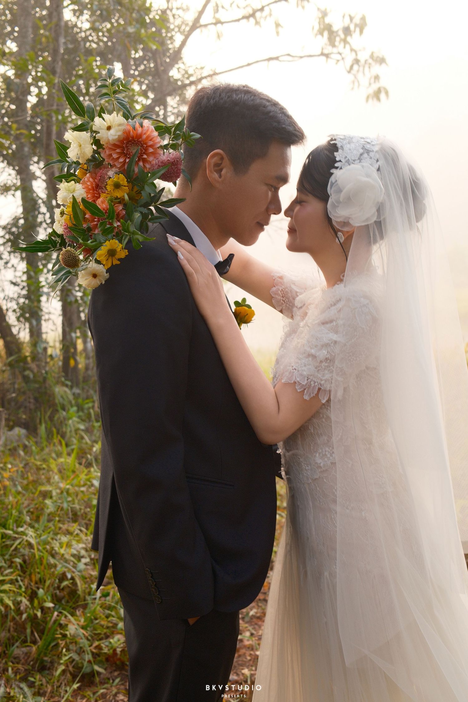 A bride and groom share an intimate moment surrounded by colorful flowers in a misty forest setting.