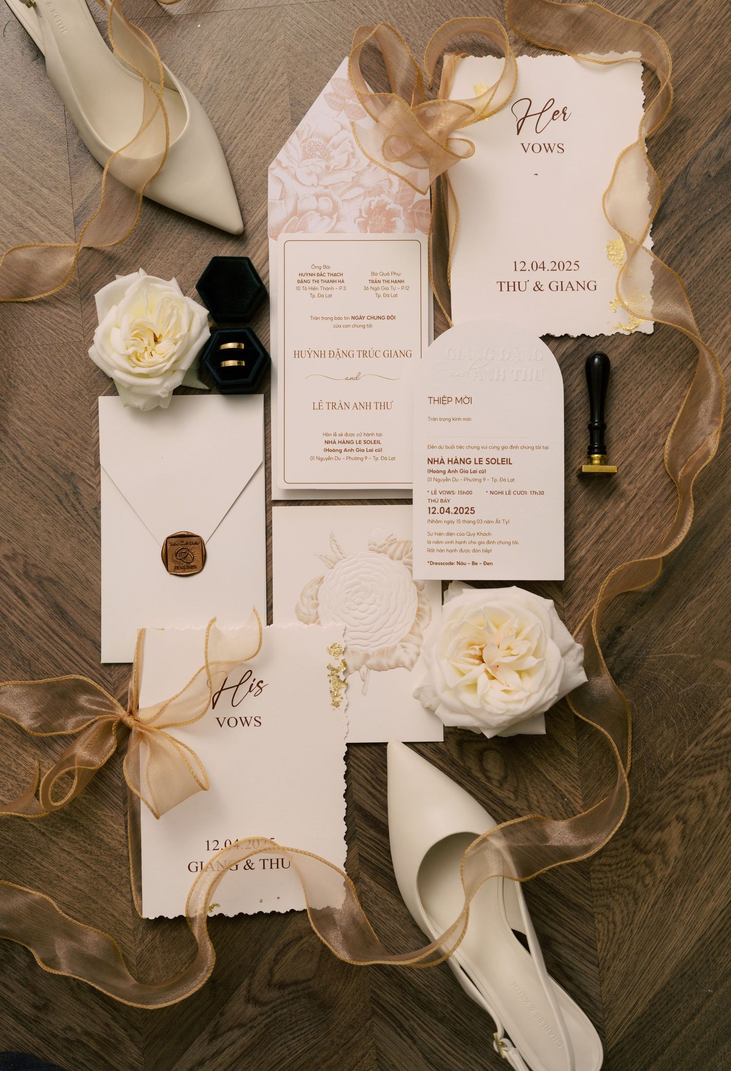 Elegant wedding stationery suite with vow books, invitations, wax seal envelope, white roses, and gold ribbon on wood.