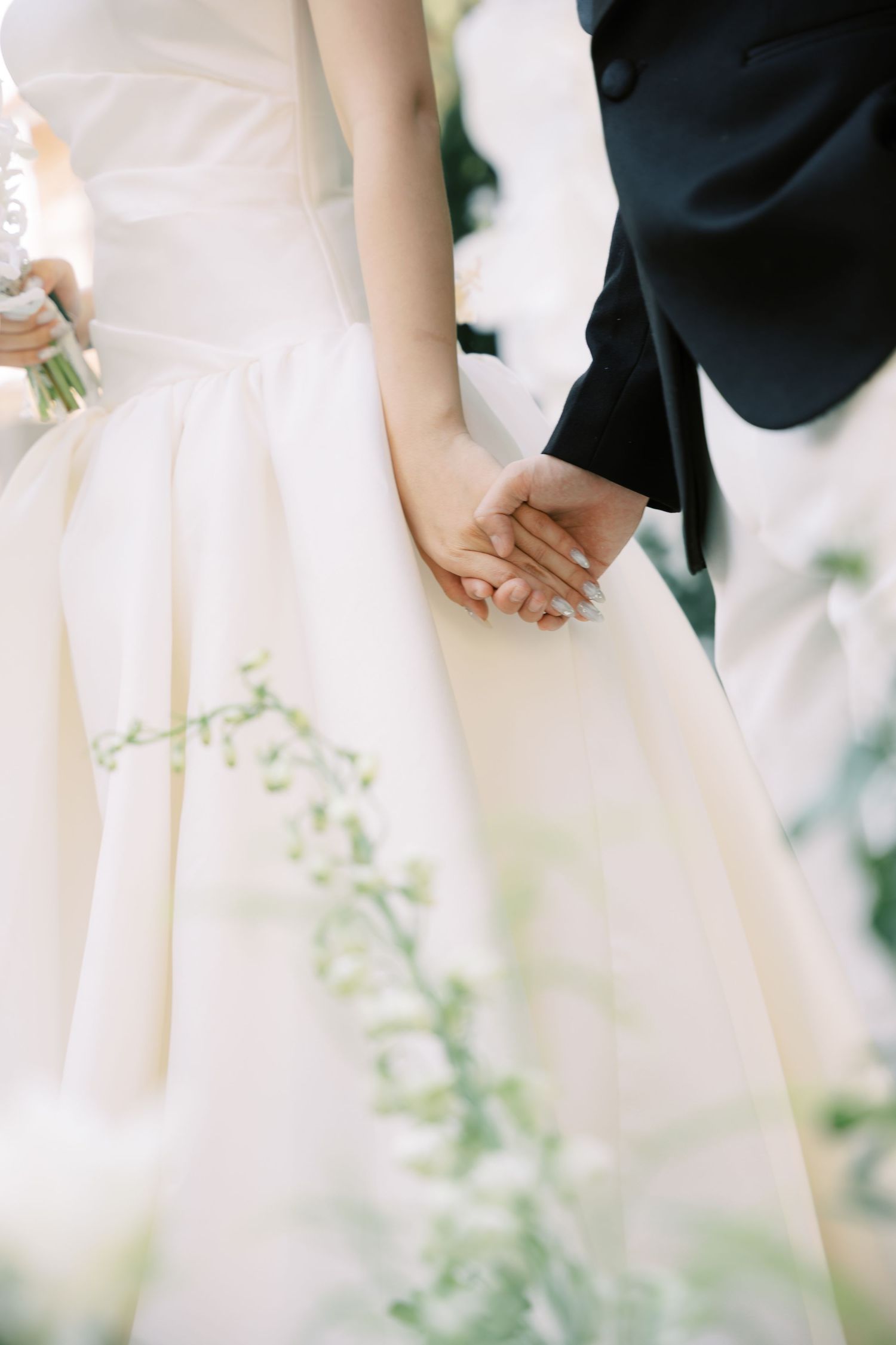 Close-up of bride and groom holding hands, bride wearing a flowing white satin wedding gown.