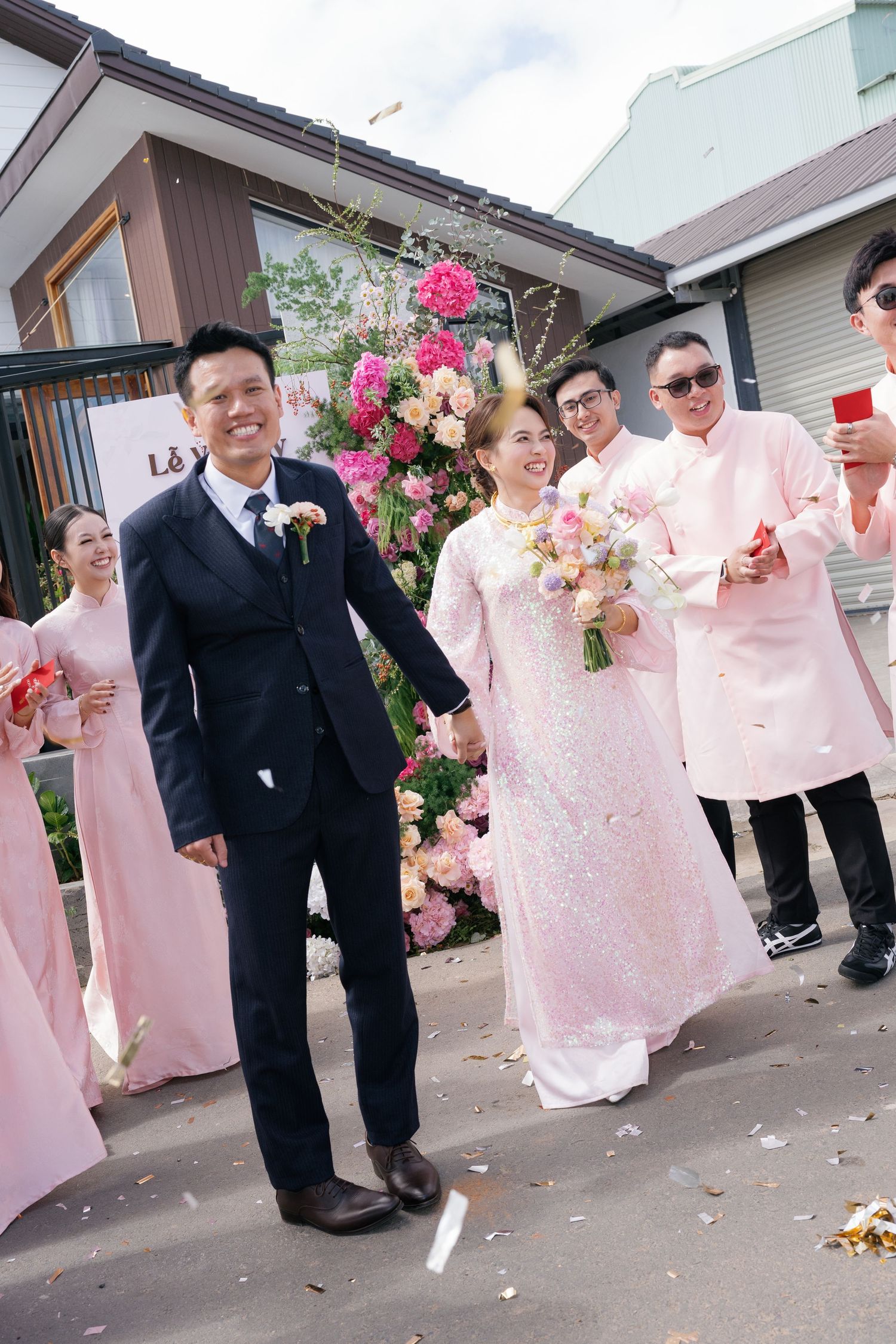 Vietnamese bride in pink ao dai and groom walking hand in hand with wedding party.