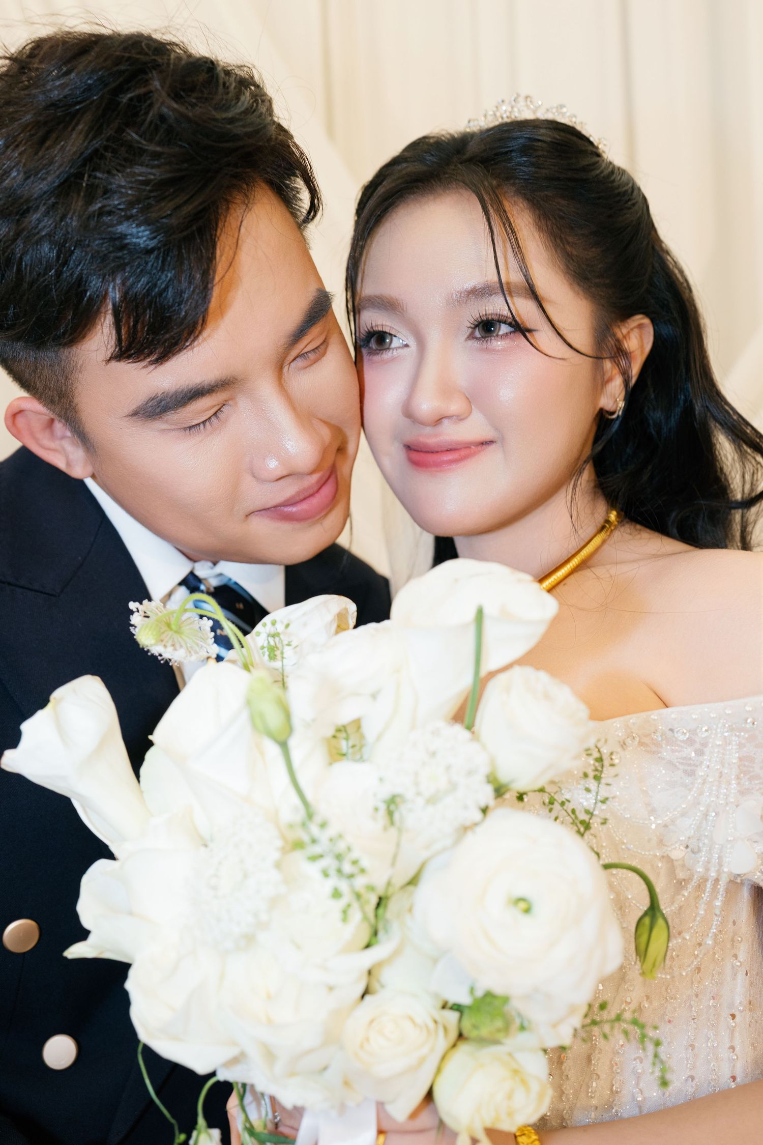 Vietnamese bride and groom sharing tender moment holding white rose bouquet.