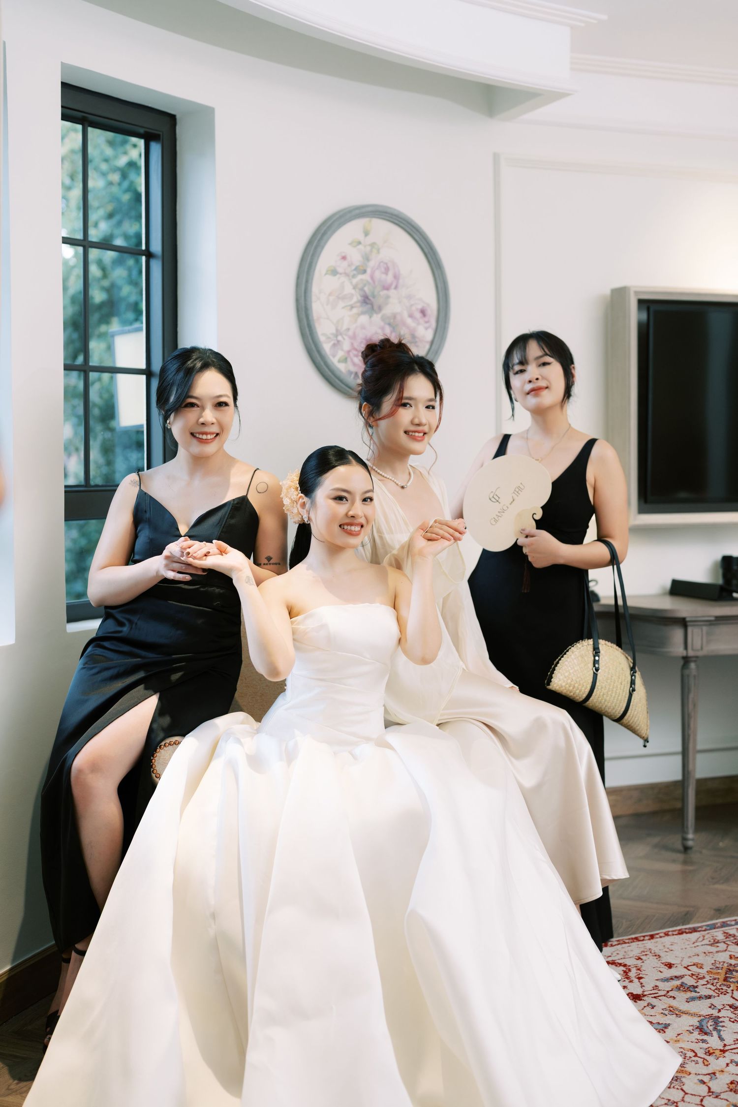 Bride in white gown poses with three bridesmaids in black dresses indoors before the ceremony.