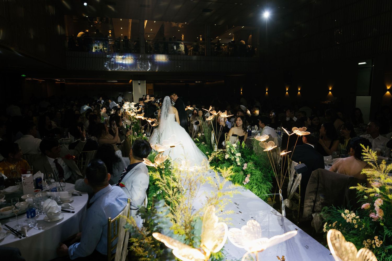 Elegant wedding reception with bride and groom walking down a floral aisle surrounded by guests at candlelit tables.
