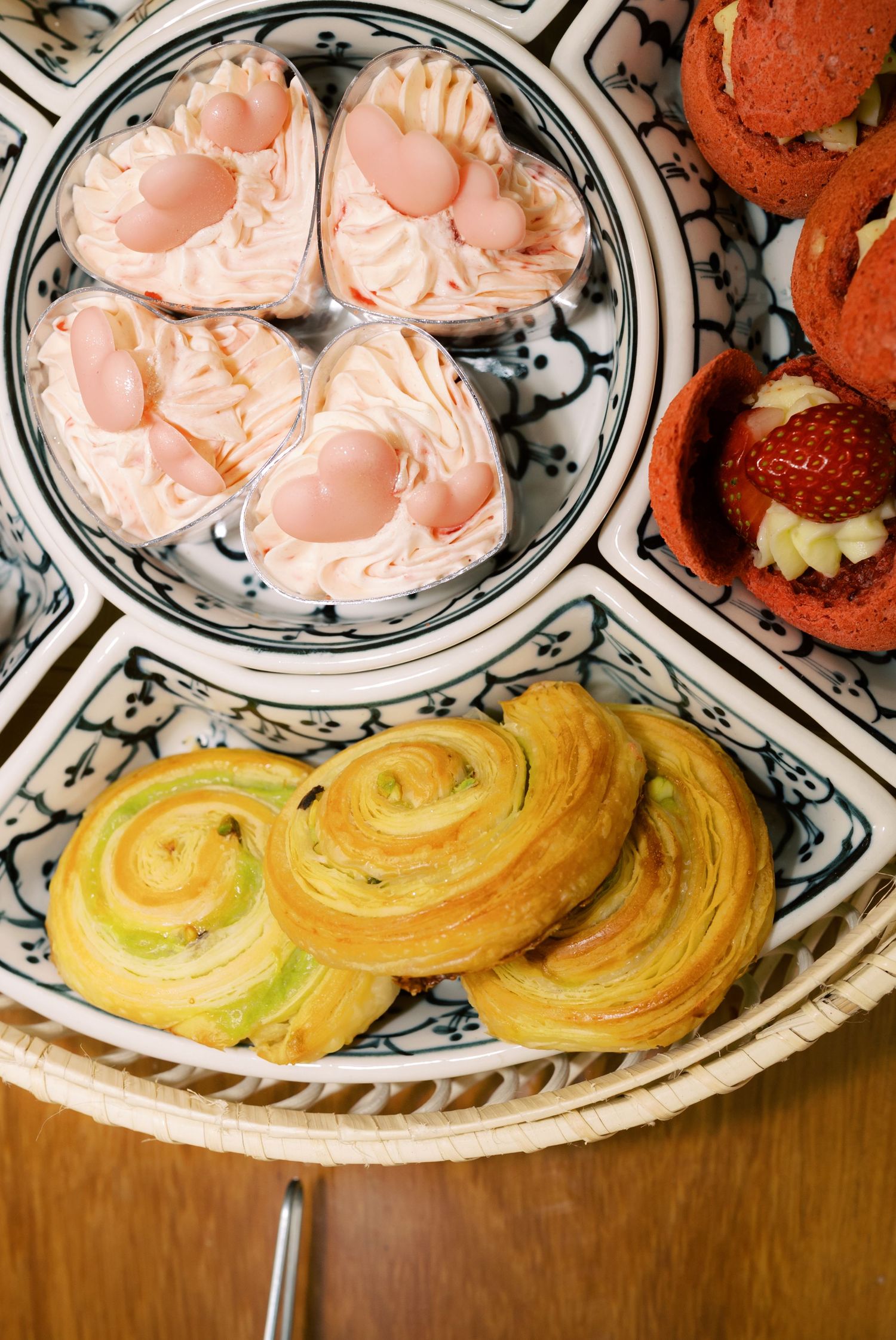 Assorted Vietnamese pastries including spiral pandan cookies, pink cream desserts, and strawberry cakes on decorative blue and white plates.