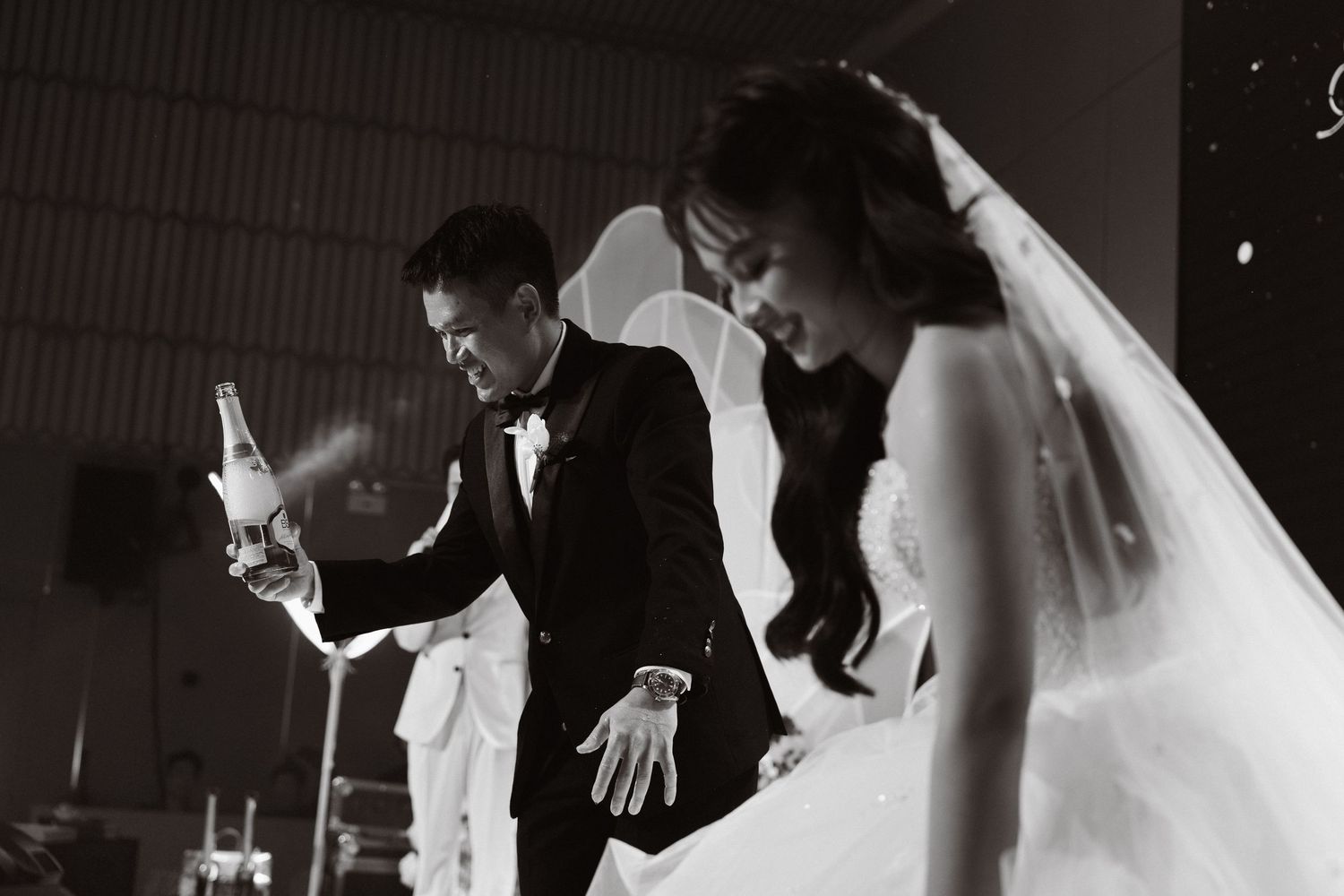 Black and white wedding photo of bride in veil and groom in tuxedo during a candlelit ceremony.