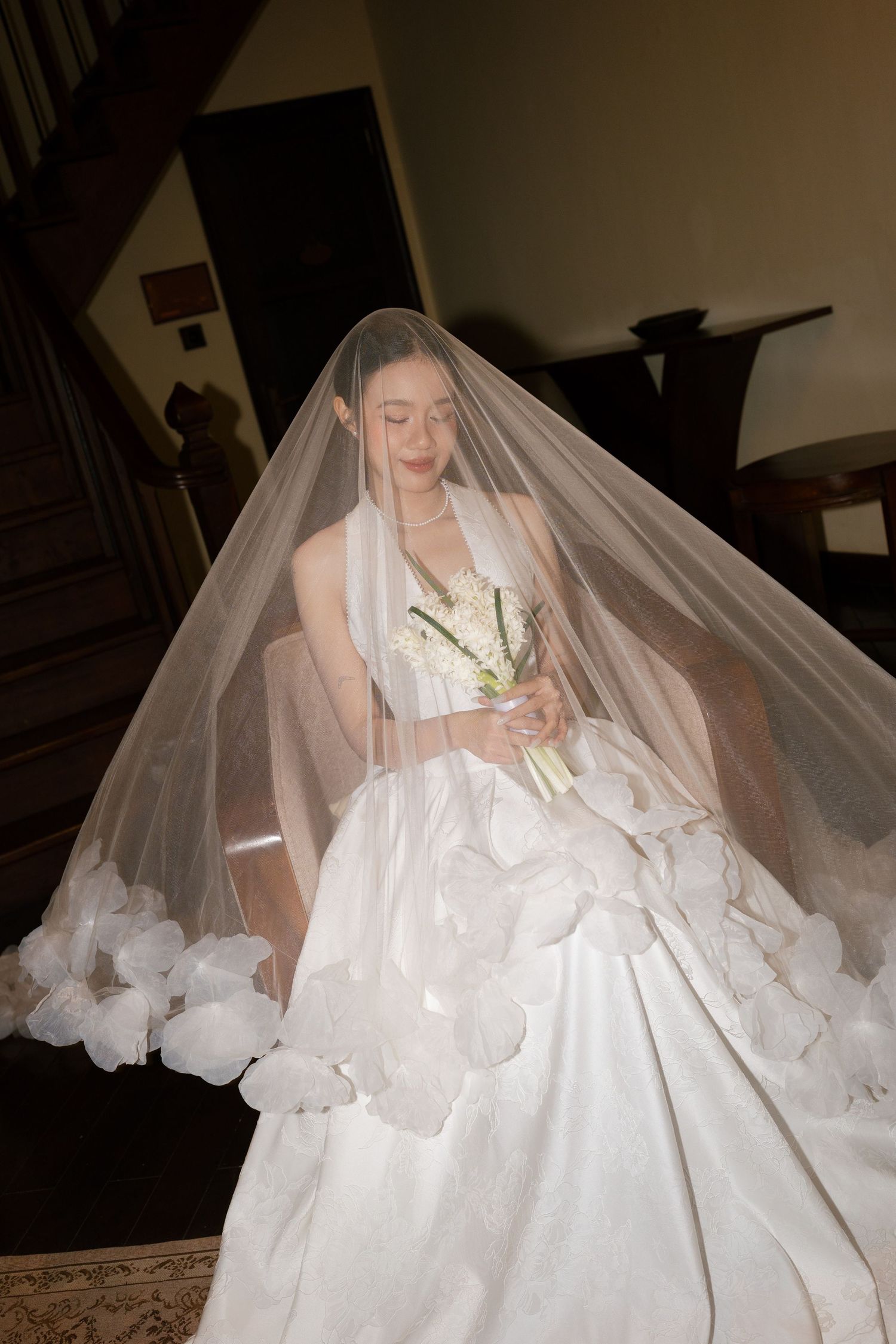 Bride in voluminous white wedding dress and long veil holding white floral bouquet on staircase.