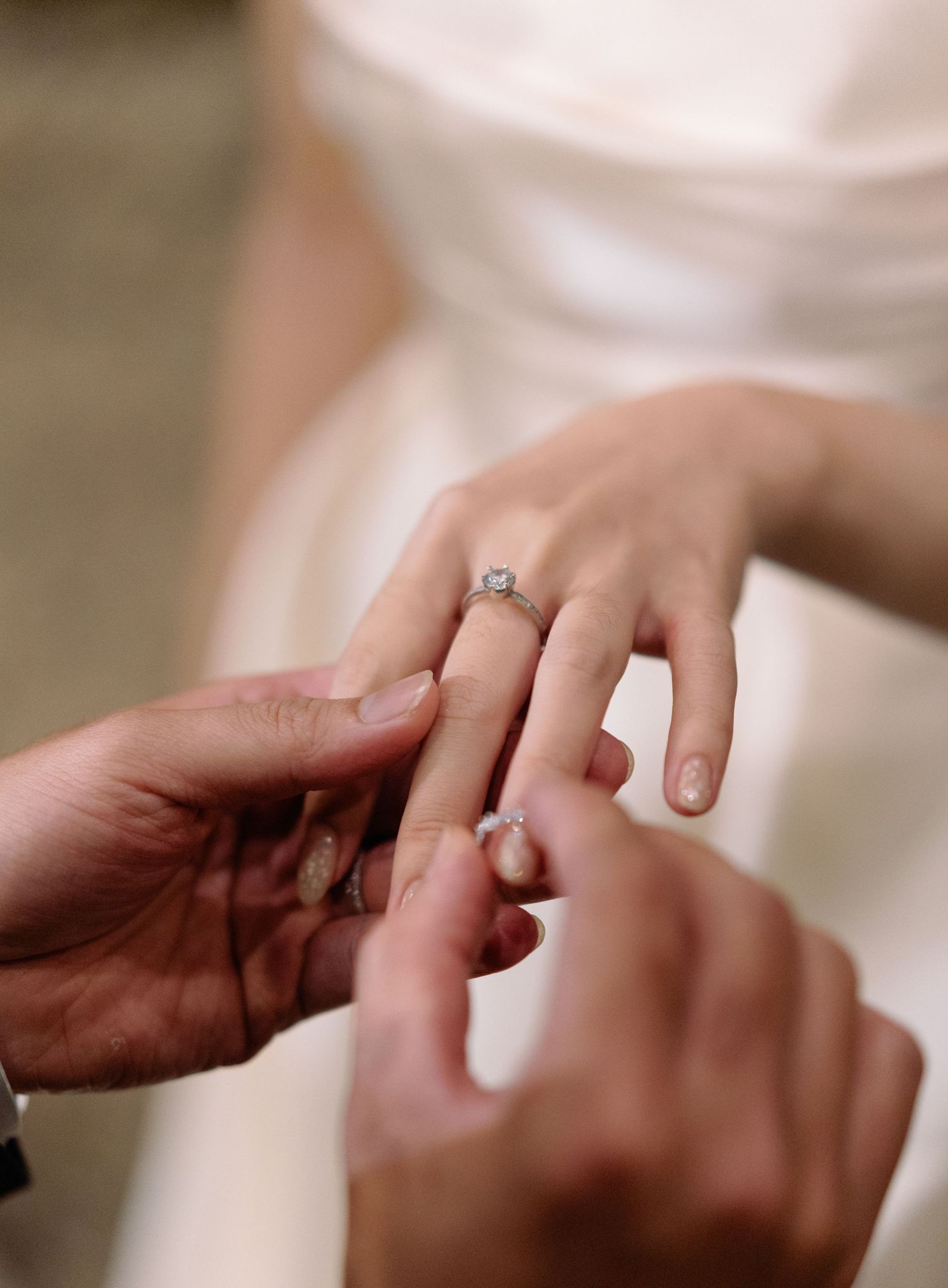 Close-up of groom placing diamond engagement ring on bride's finger during wedding ring exchange ceremony.