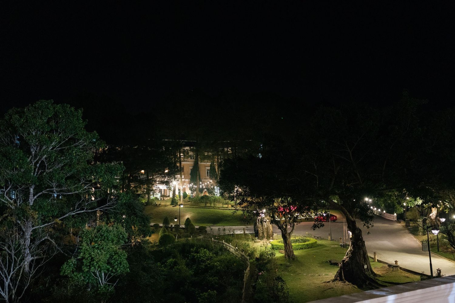 Night view of illuminated garden and historic building surrounded by trees under a dark sky.