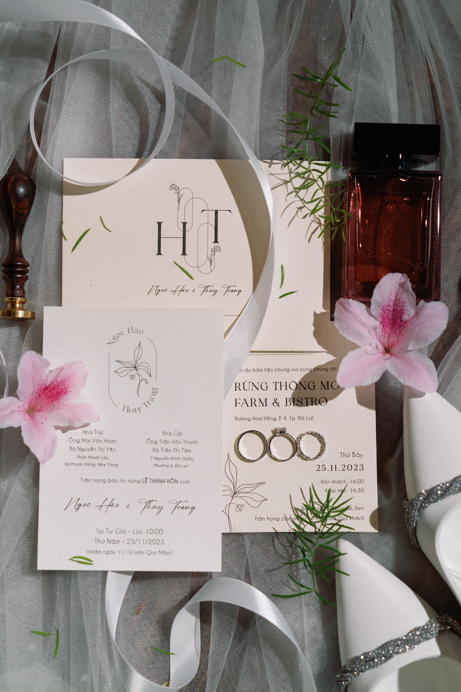 Wedding stationery flat lay with HT monogram invitations, gold rings, pink flowers, and ribbon details.