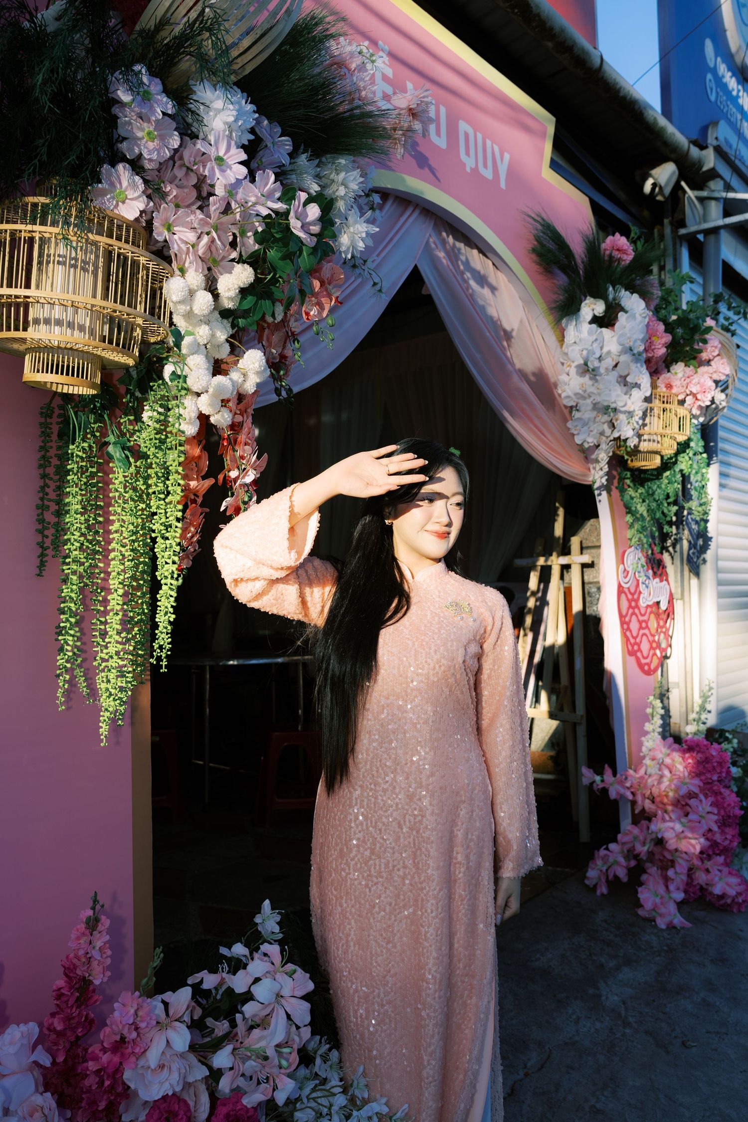 Vietnamese bride in sequined pink ao dai poses under floral arch entrance at wedding venue.