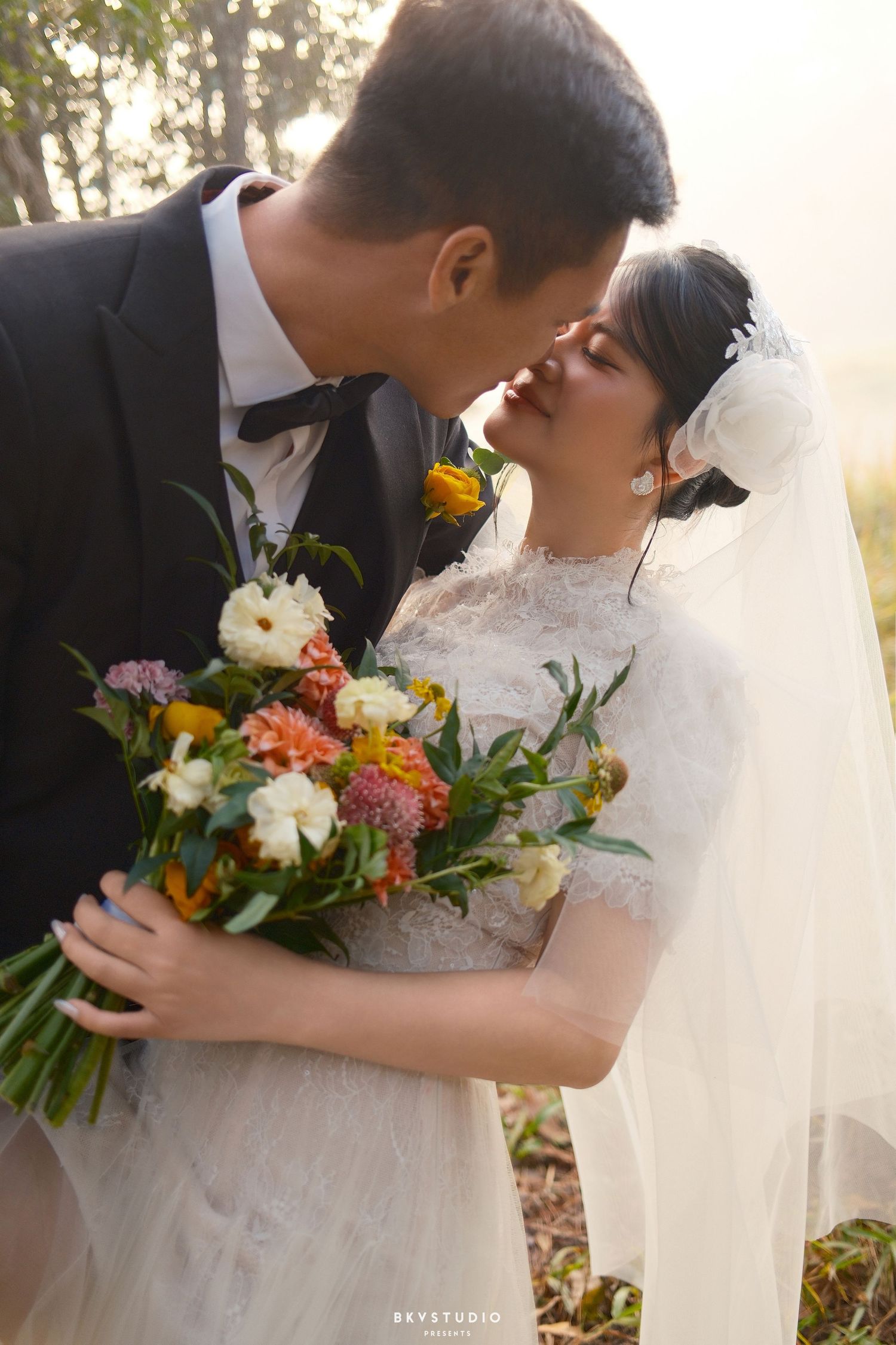 Couple shares a romantic almost-kiss moment as bride holds colorful bridal bouquet in golden outdoor light.