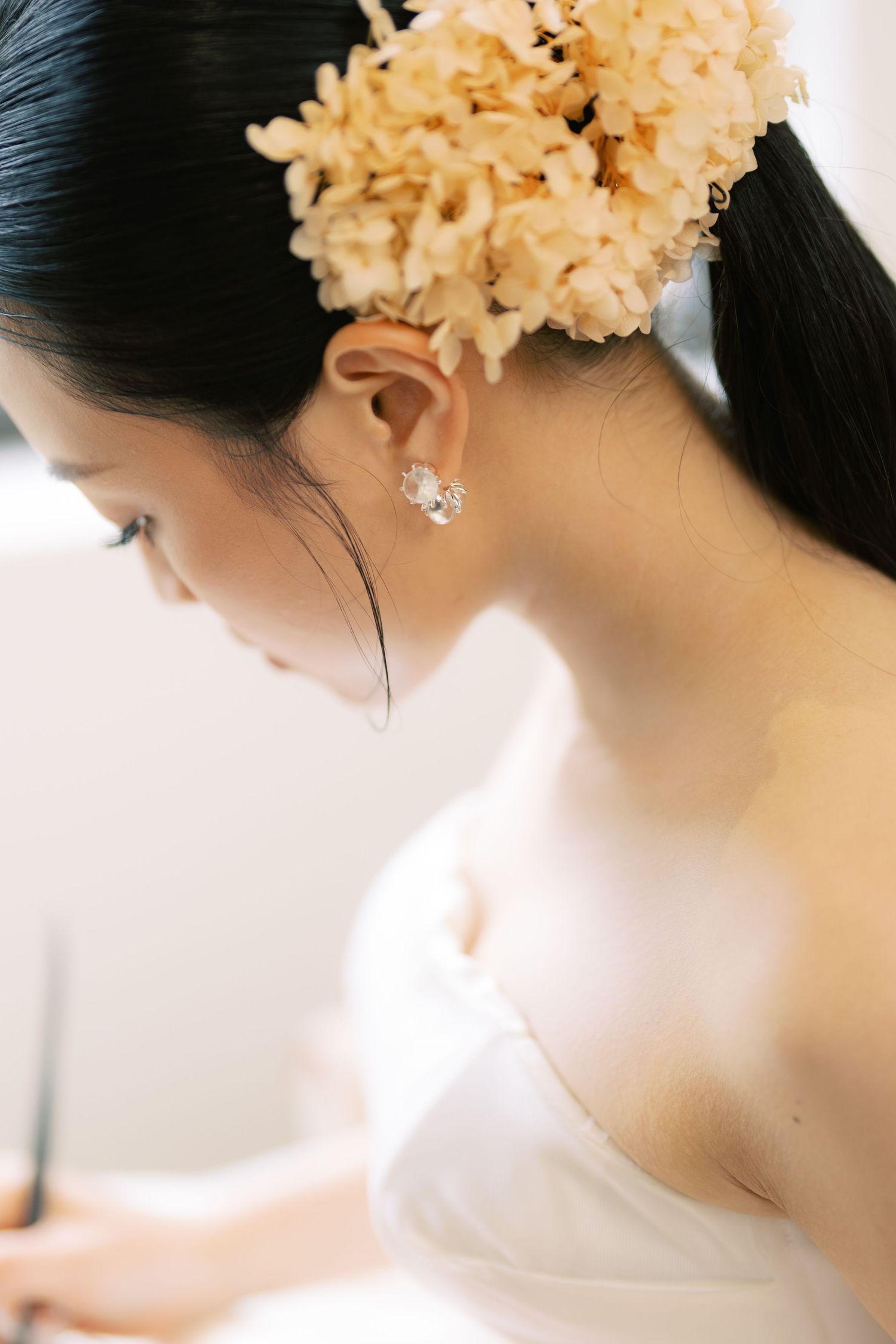 A bride with dark hair adorned with dried hydrangeas wearing a crystal earring and white strapless dress.
