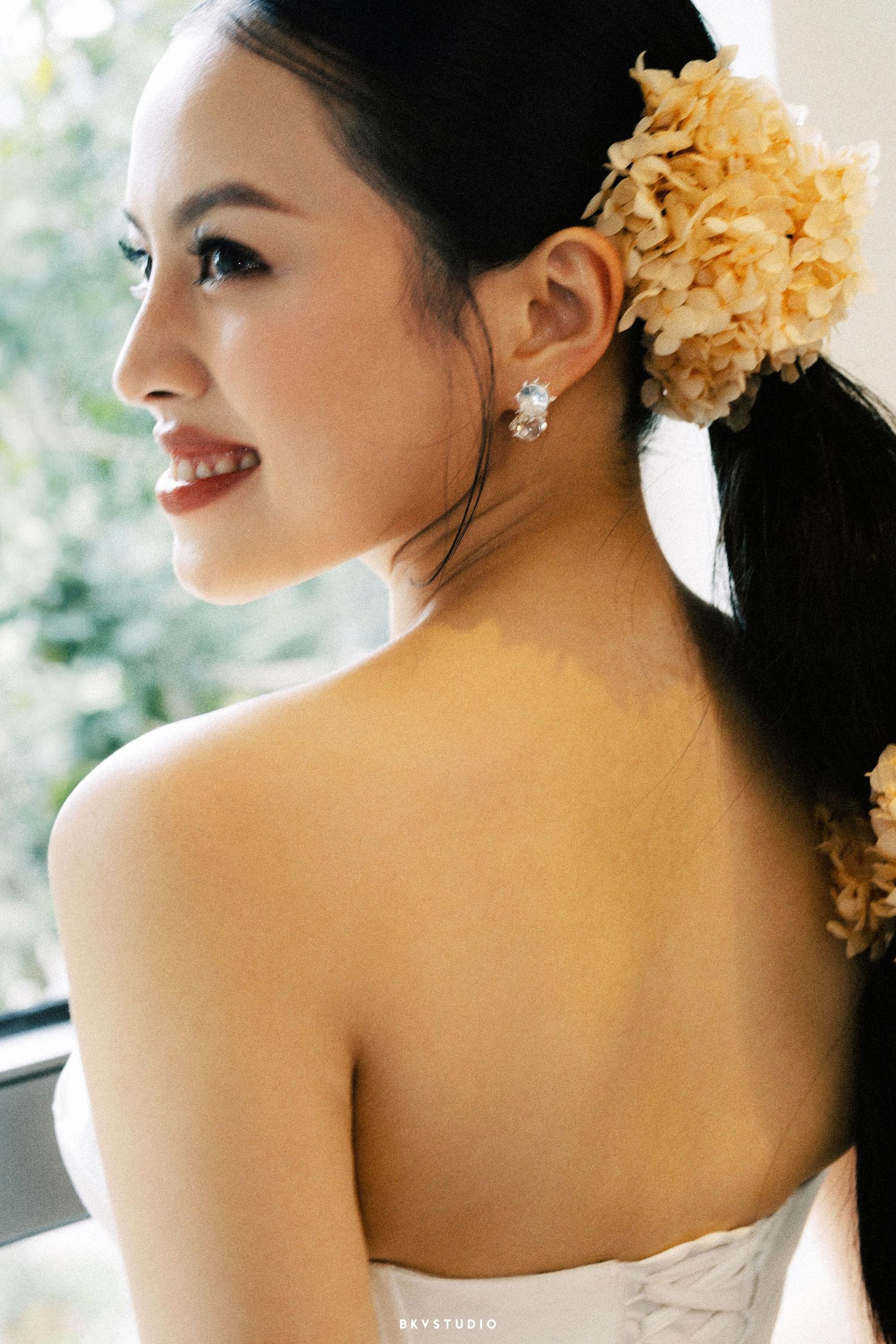 Asian bride with floral hair accessory and pearl earrings in strapless wedding gown.