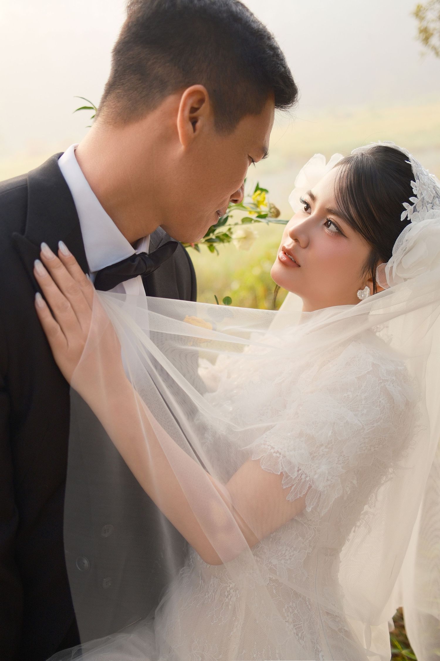 Bride gazing up at groom in an intimate outdoor moment with veil flowing in sunlight.