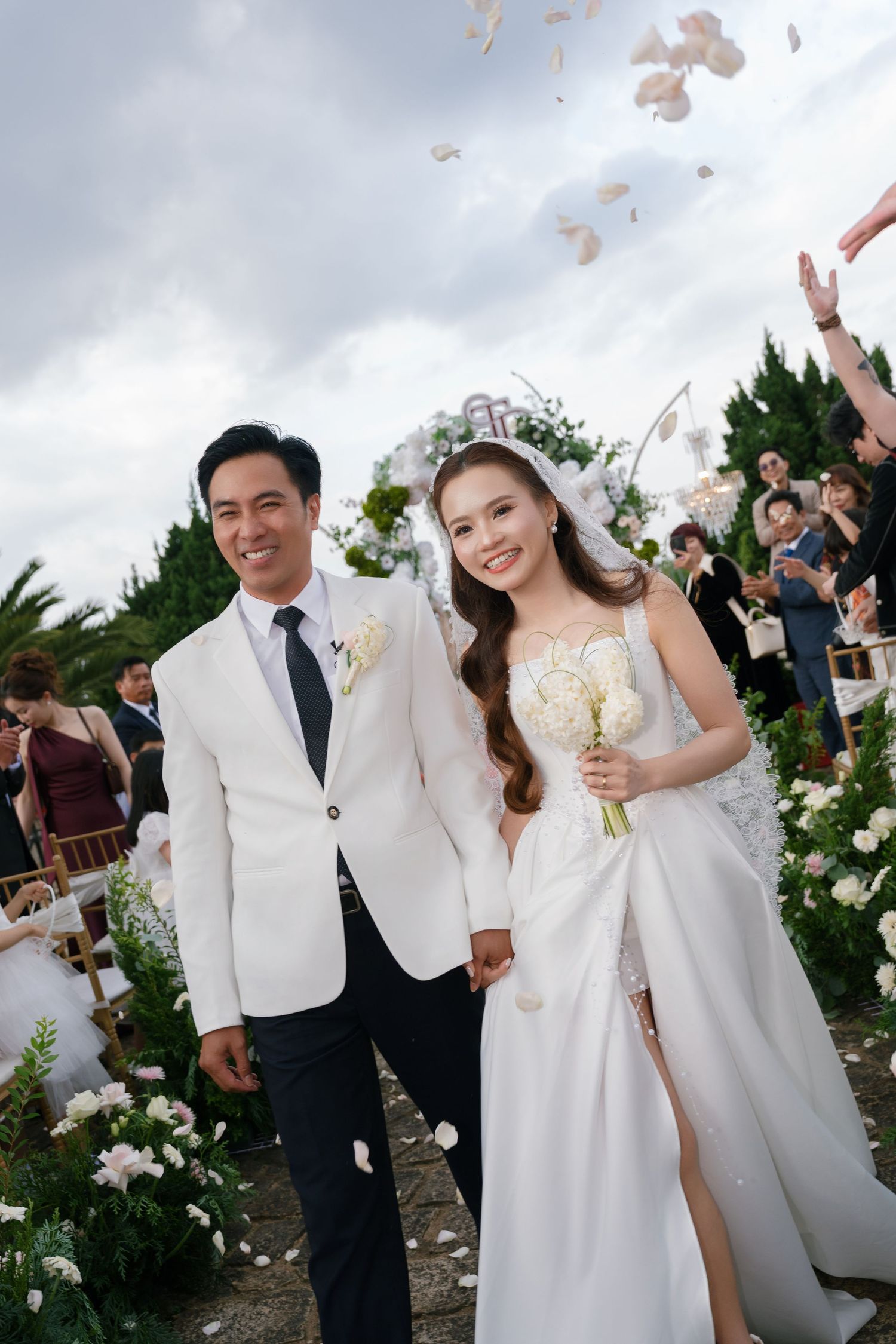 A joyful newlywed couple walks down the aisle as flower petals rain down at their outdoor garden wedding.