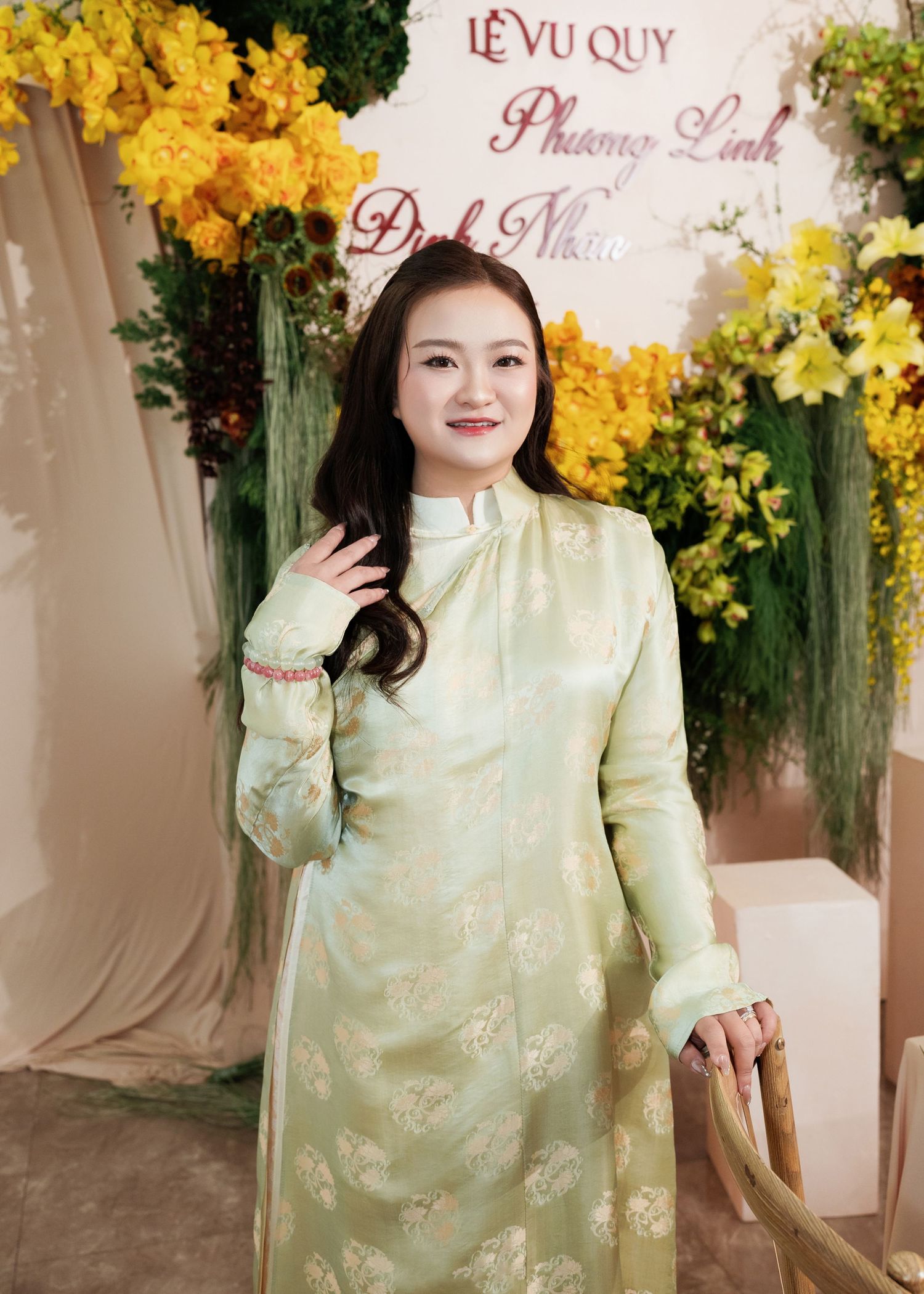 Woman in light green floral ao dai at a Vietnamese wedding ceremony with yellow flower decorations.