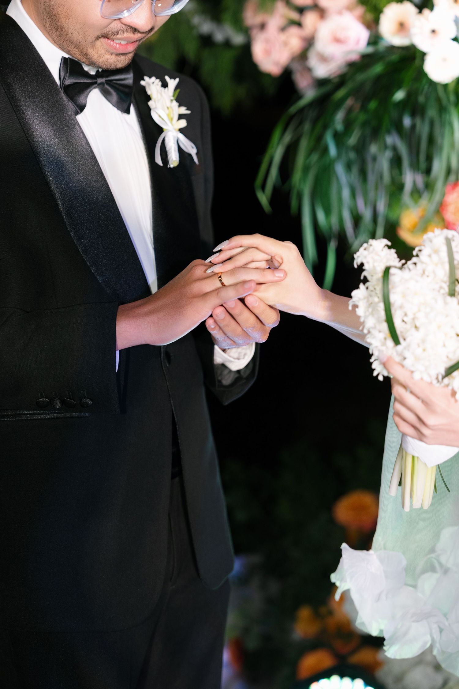 Groom places wedding ring on bride's finger during outdoor nighttime wedding ceremony.