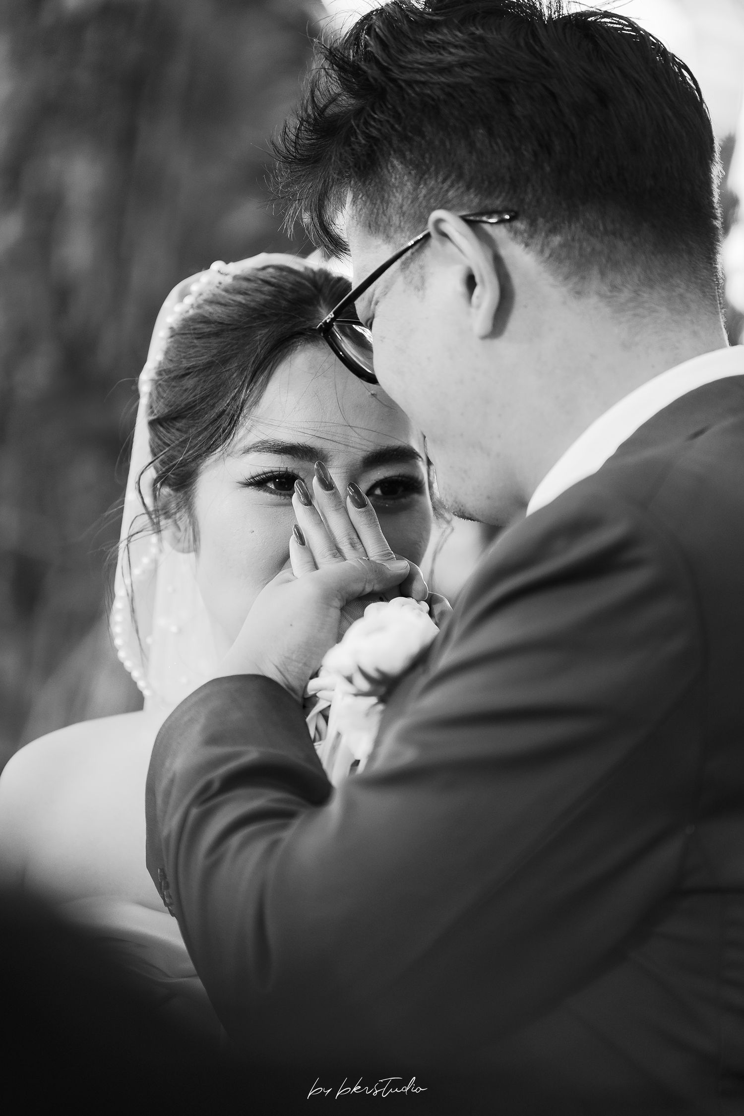 Emotional black and white photo of a bride wiping tears as groom tenderly touches her face during wedding ceremony.