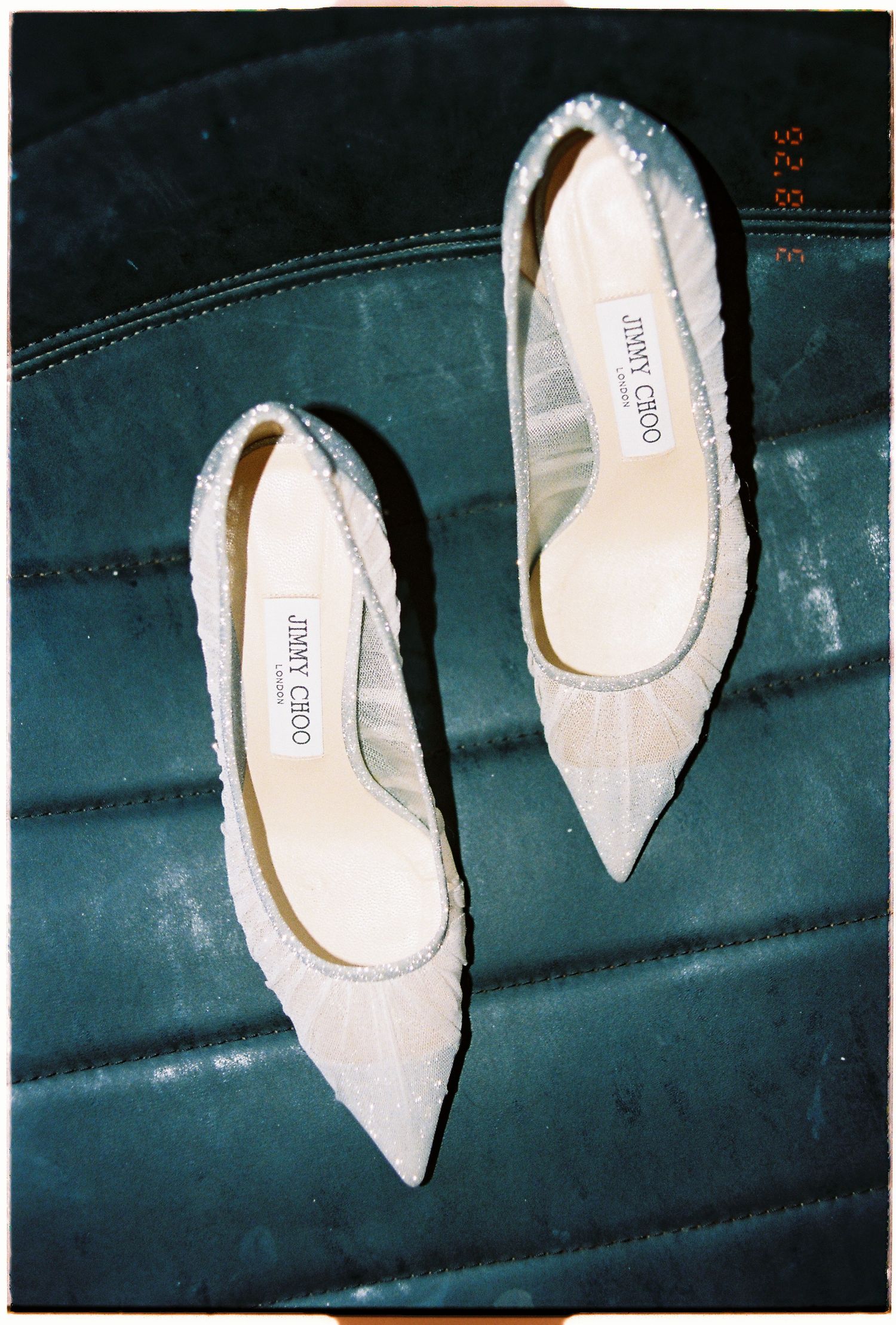 Elegant white pointed-toe Jimmy Choo slingback heels displayed on a luxurious teal velvet surface.