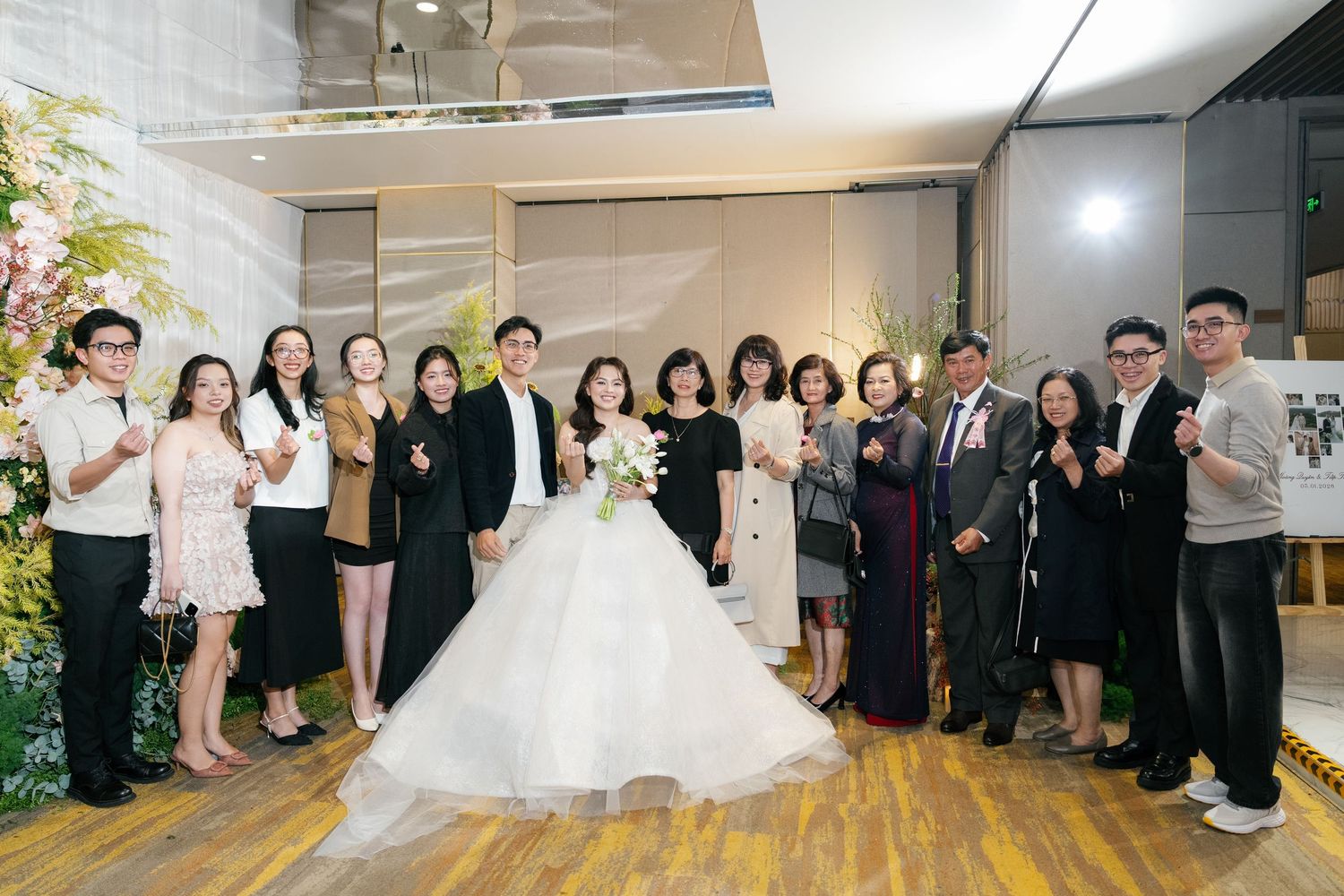 Wedding couple in white gown and suit posing with guests at elegant floral reception venue.