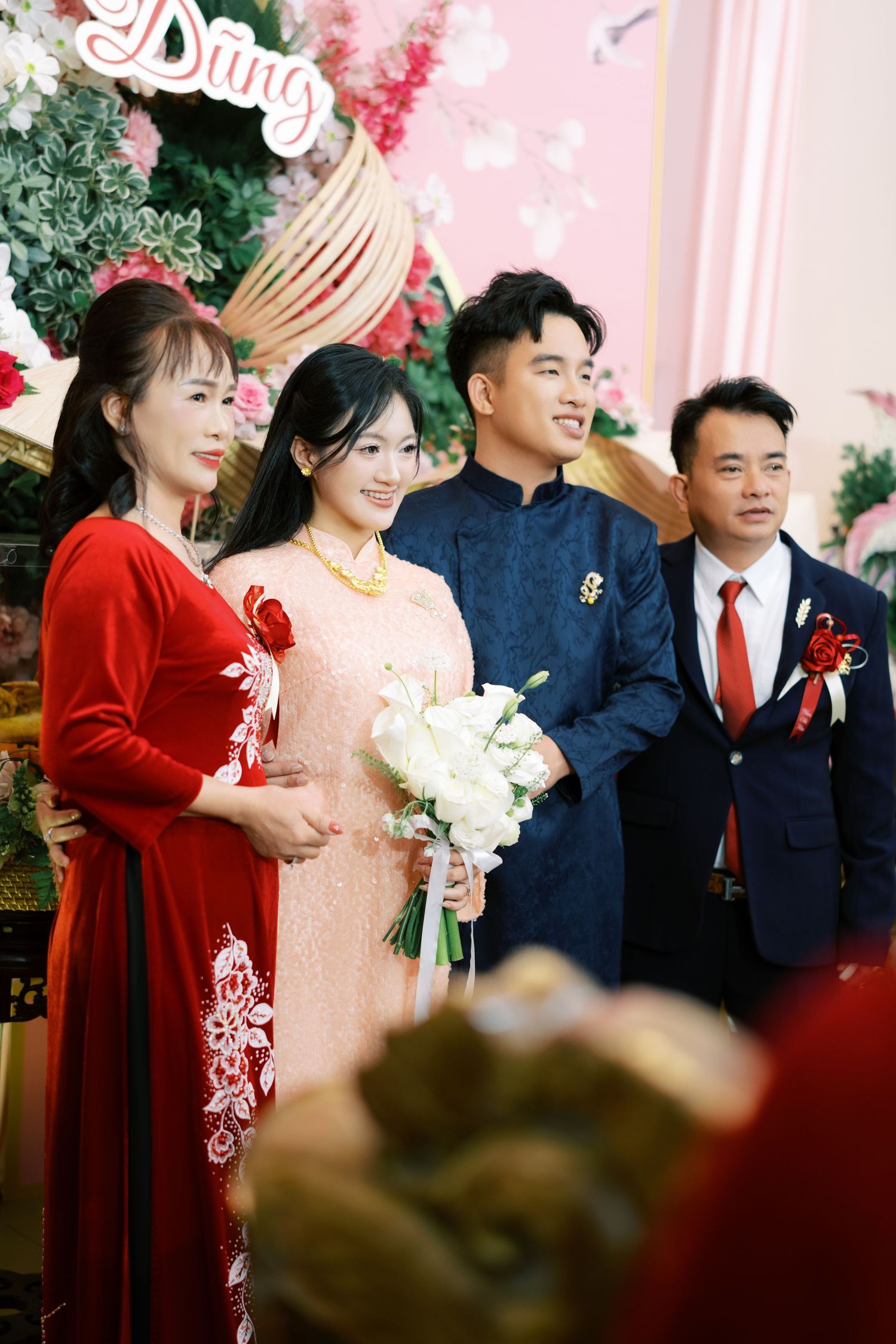Vietnamese wedding party with bride in pink ao dai and groom in blue ao dai posing with family members.