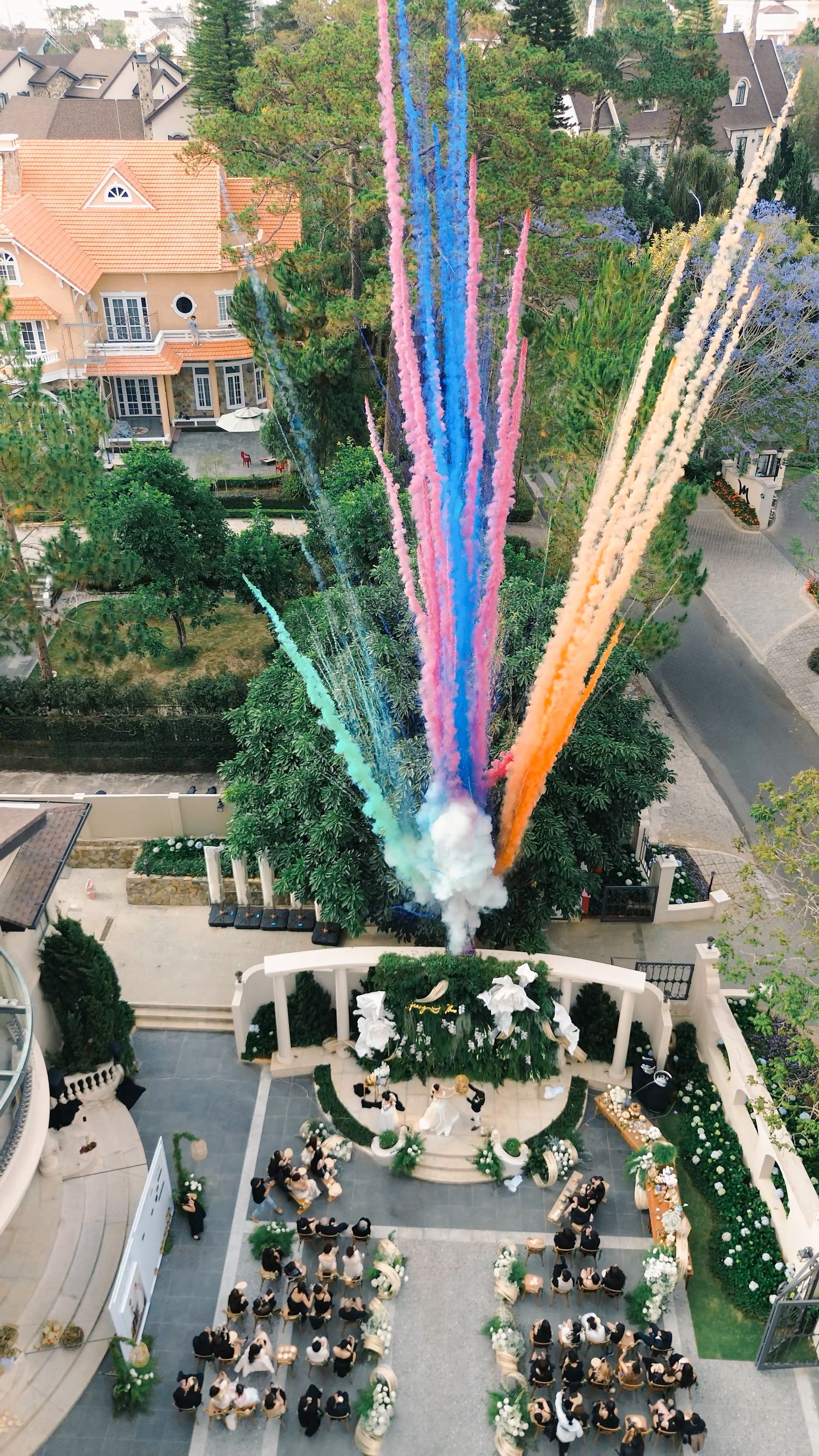 Aerial view of outdoor wedding ceremony with colorful smoke cannons firing into the sky.