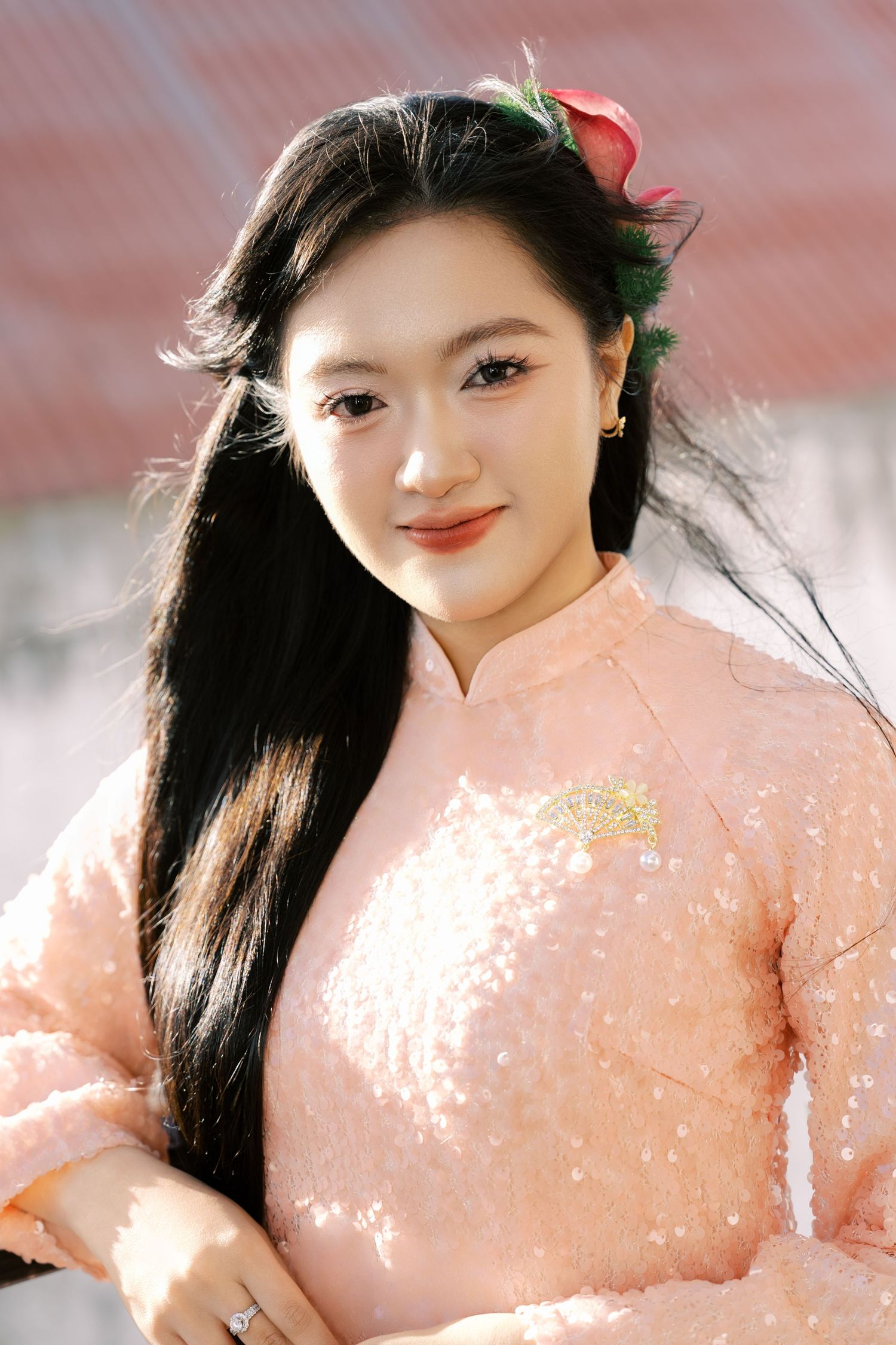 Beautiful young Vietnamese woman in a pink sequined ao dai with a red flower in her long black hair.