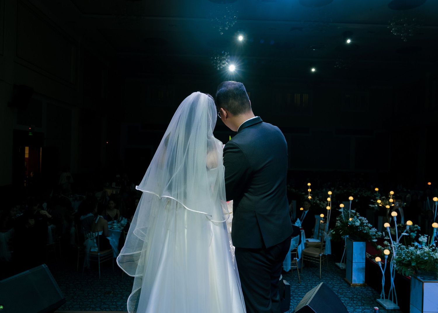 Bride and groom share an intimate moment at the altar during a candlelit wedding ceremony with guests seated in background.