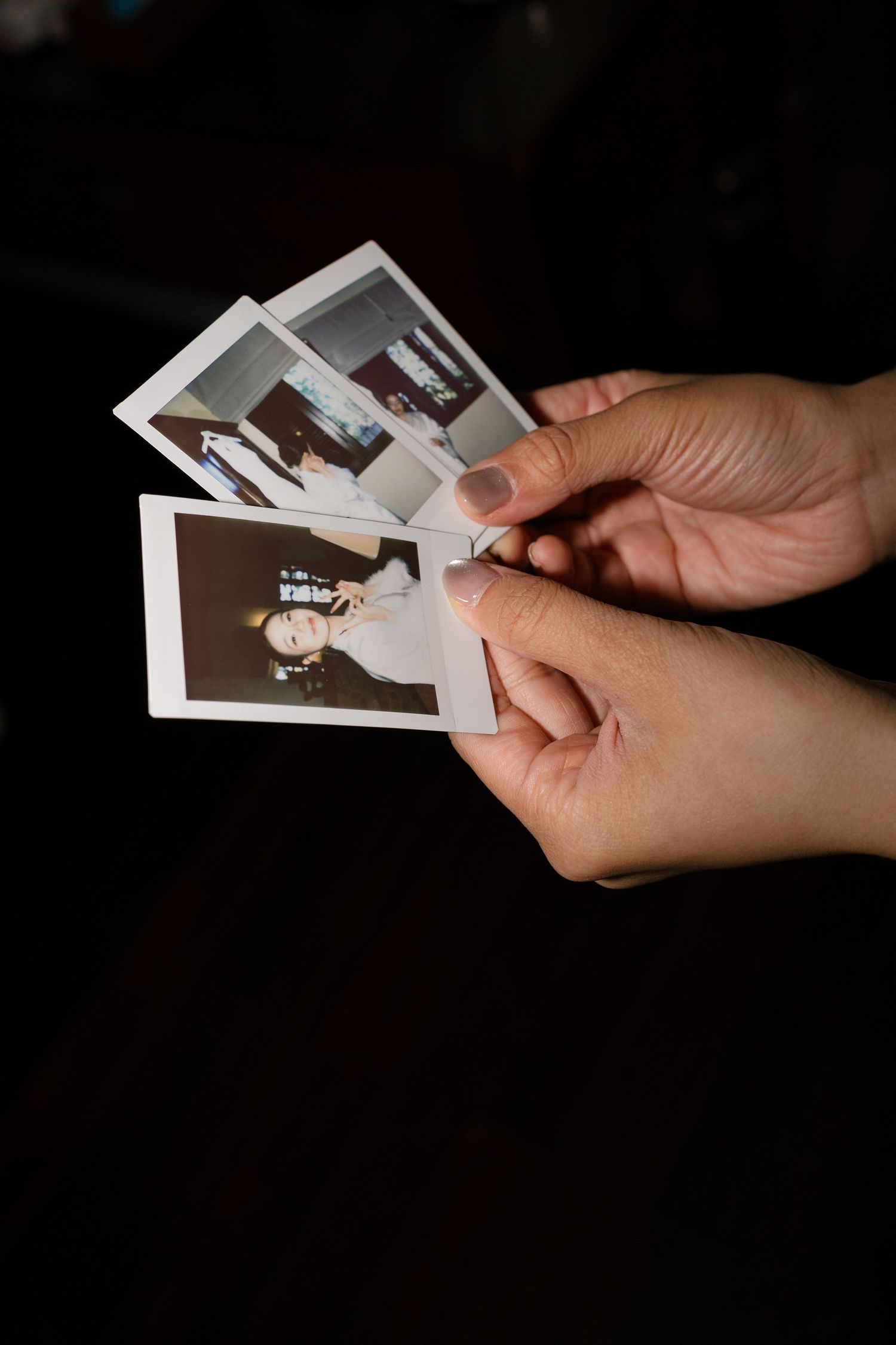 Hands holding multiple Polaroid instant photos of a bride at a wedding celebration.