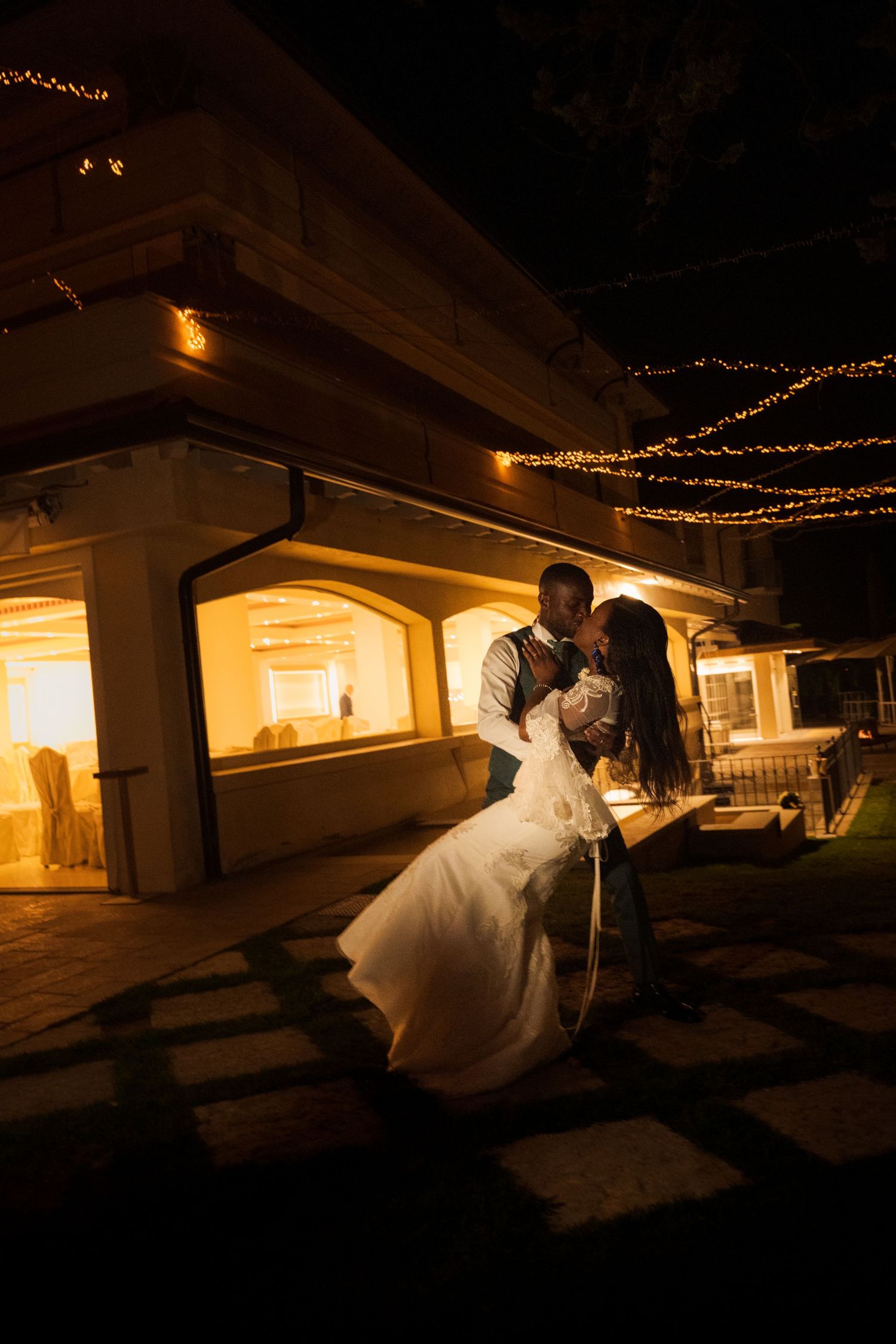 Bride and groom share a romantic dance outdoors at night, surrounded by warm string lights at their wedding venue.