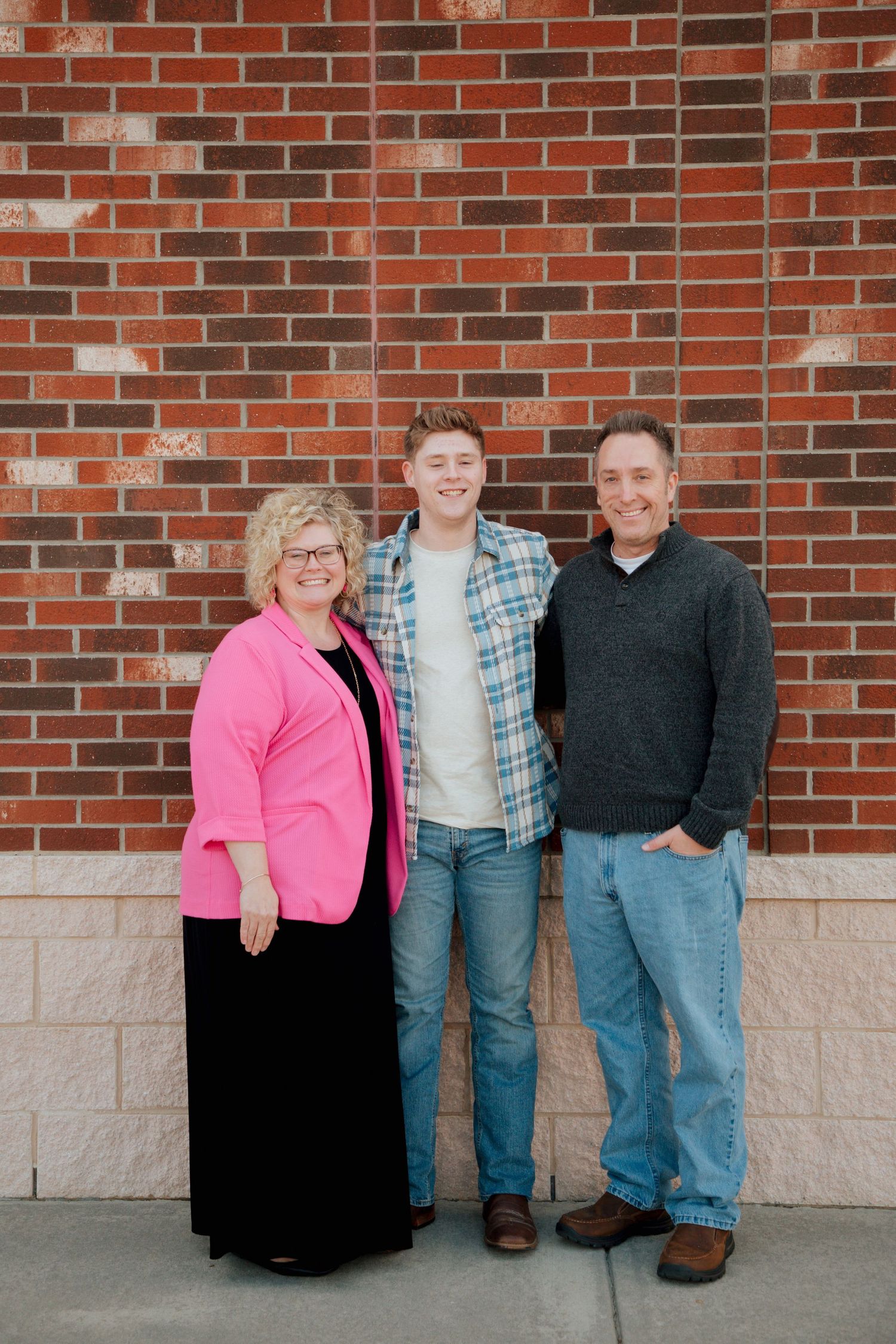 Family of three smiling together against red brick wall during senior photo session.