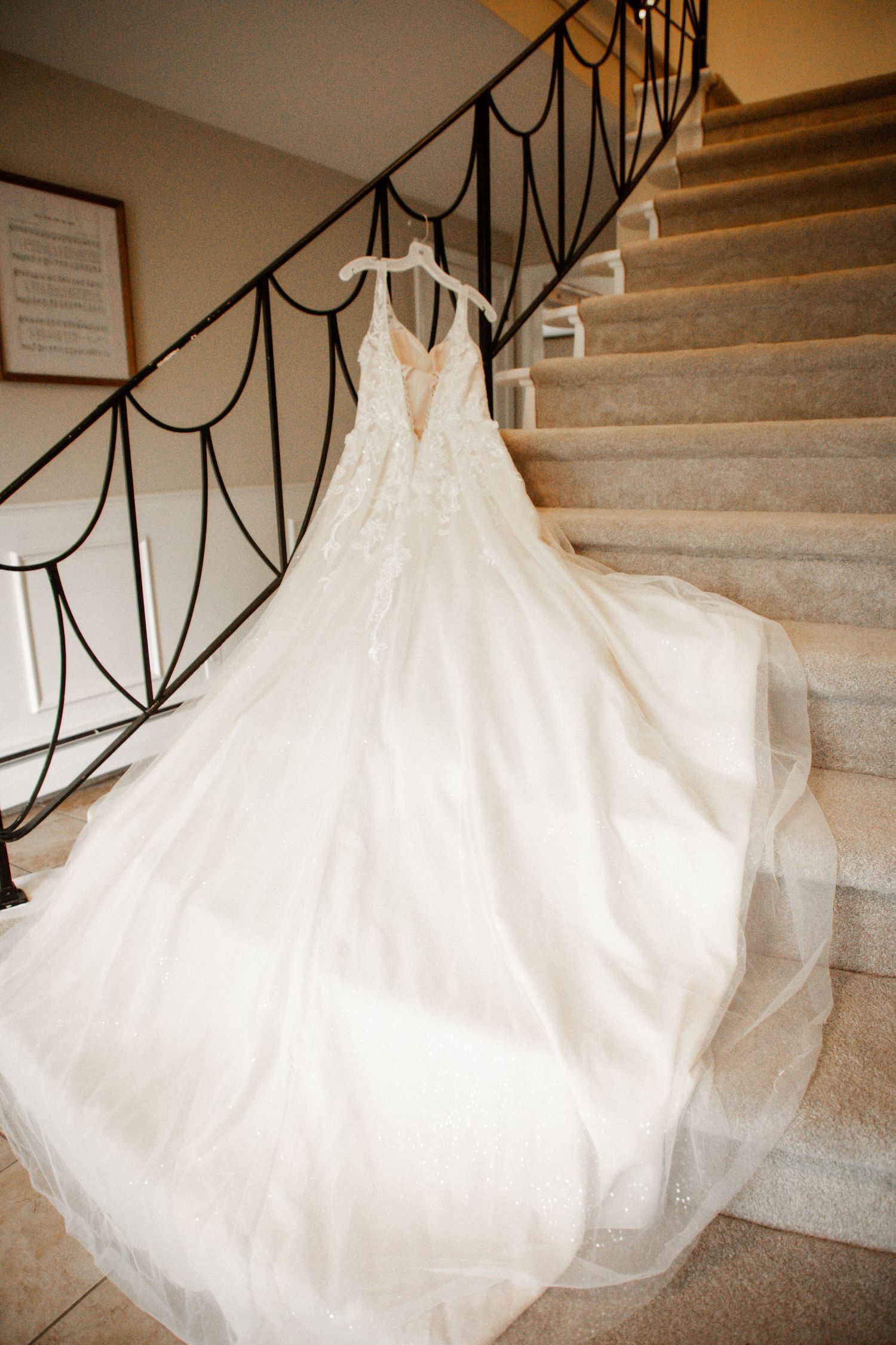 Flowing lace and tulle bridal gown with V-neckline displayed on a staircase with elegant iron railing.