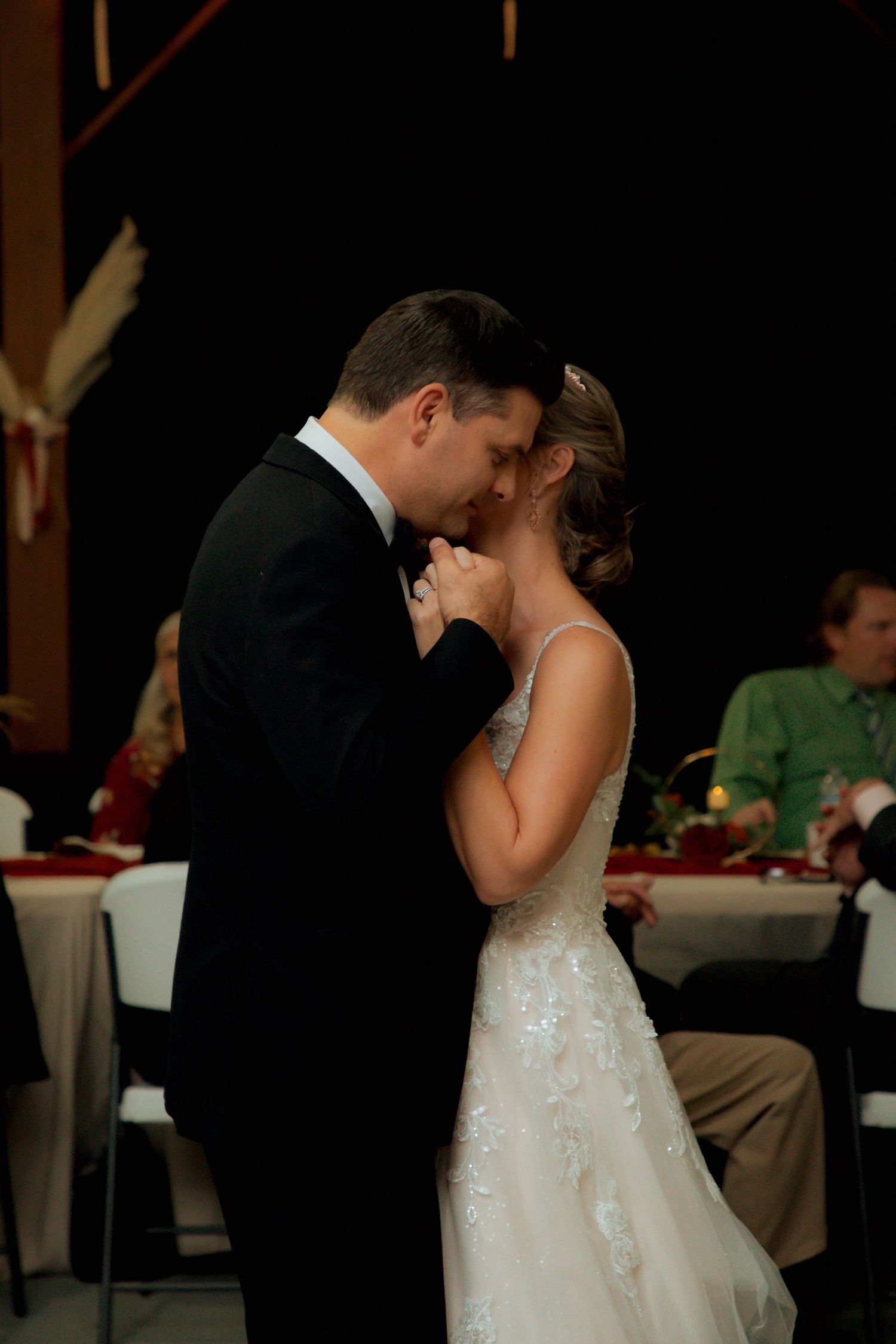 Newlyweds share an intimate first dance moment in a softly lit wedding reception hall.