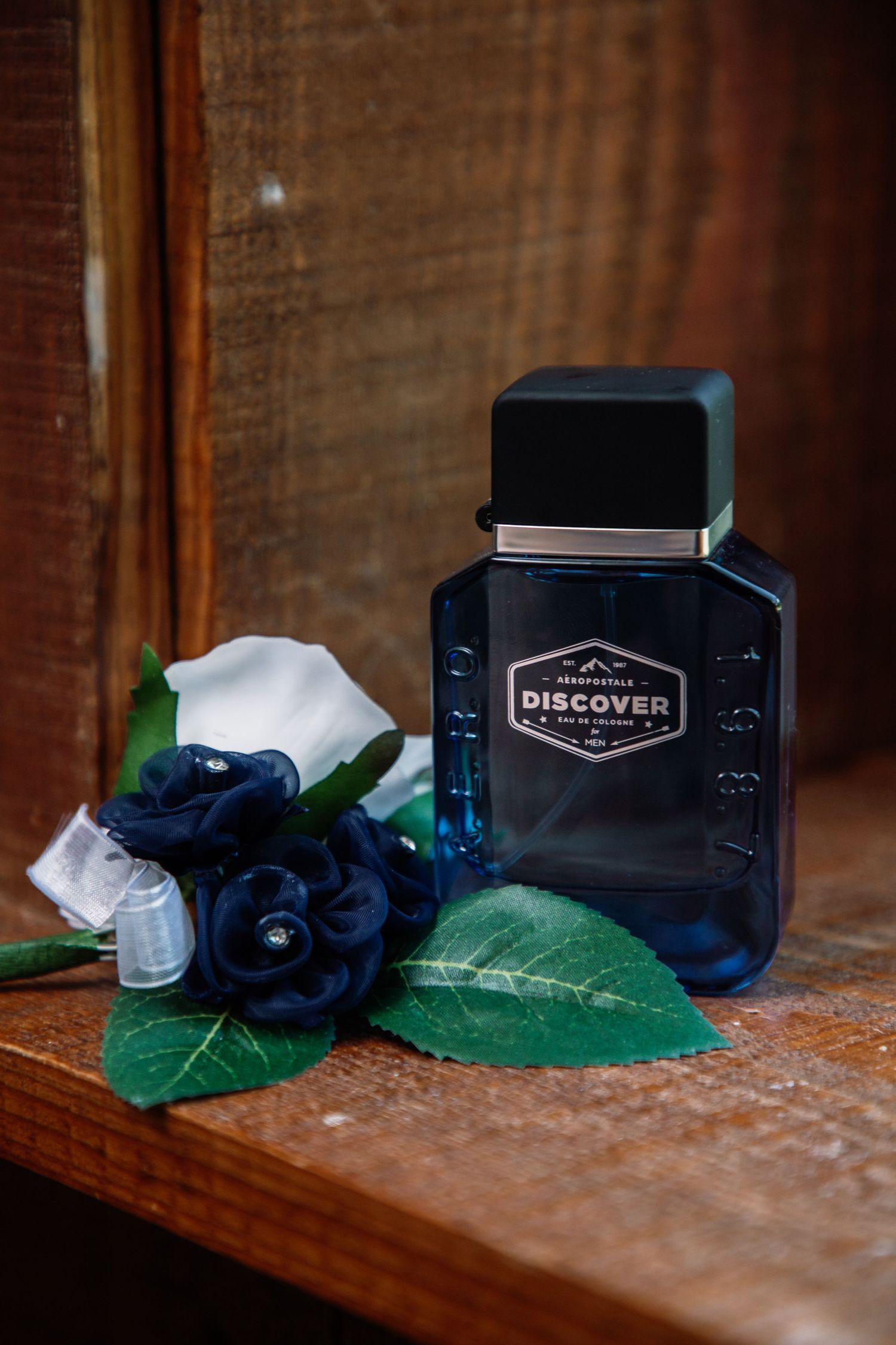 Navy blue Abercrombie Discover cologne bottle beside a navy rose boutonniere on wooden surface.