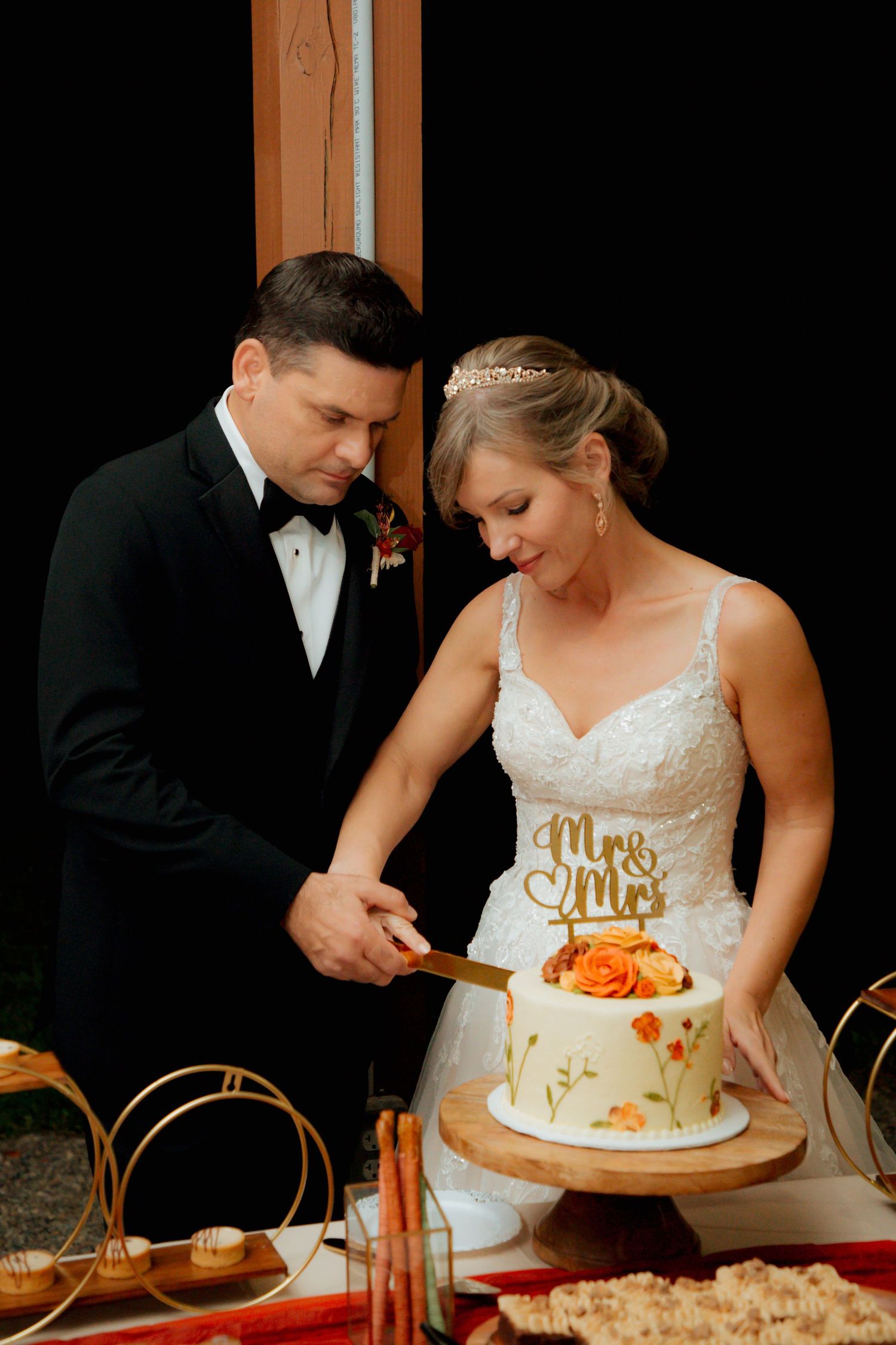 Bride and groom cut their floral wedding cake topped with a gold Mr & Mrs topper.