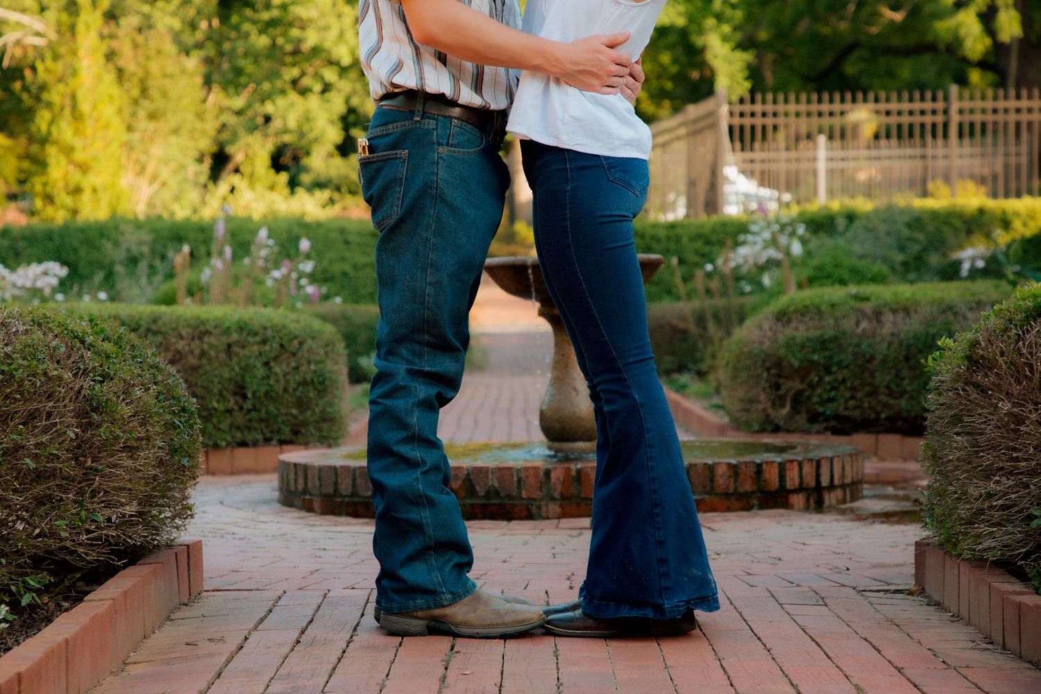 Couple standing close together on a brick pathway in a lush garden setting.