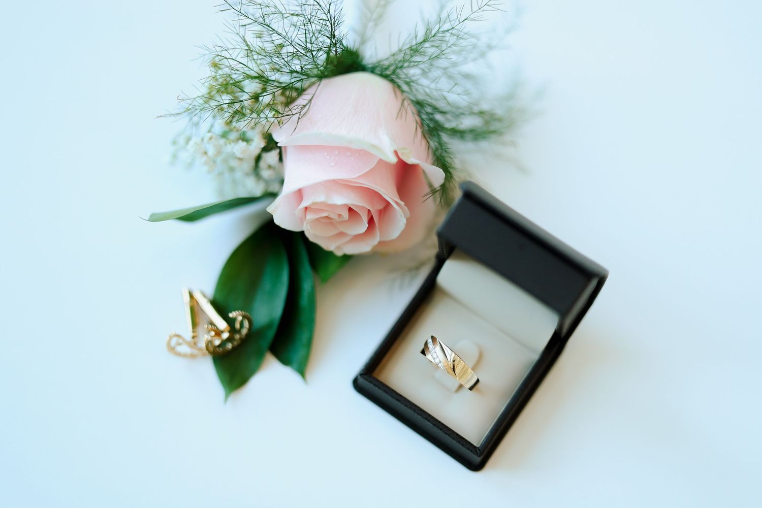 Gold butterfly cufflinks and ring set in black box beside pink rose boutonniere.